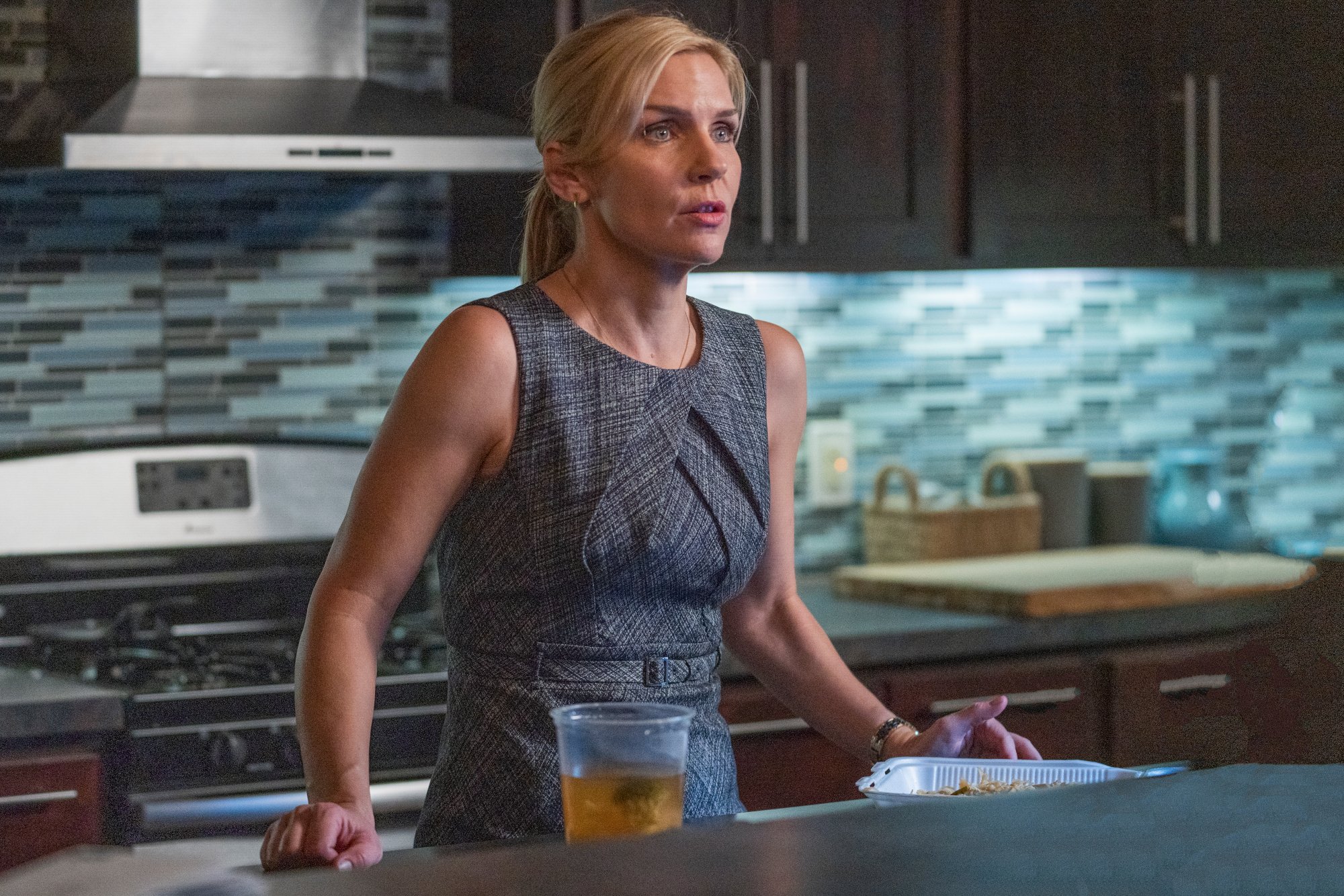 Rhea Seehorn as Kim Wexler 'Better Call Saul' Season 5. She's standing near a counter and wearing a blue tank top.