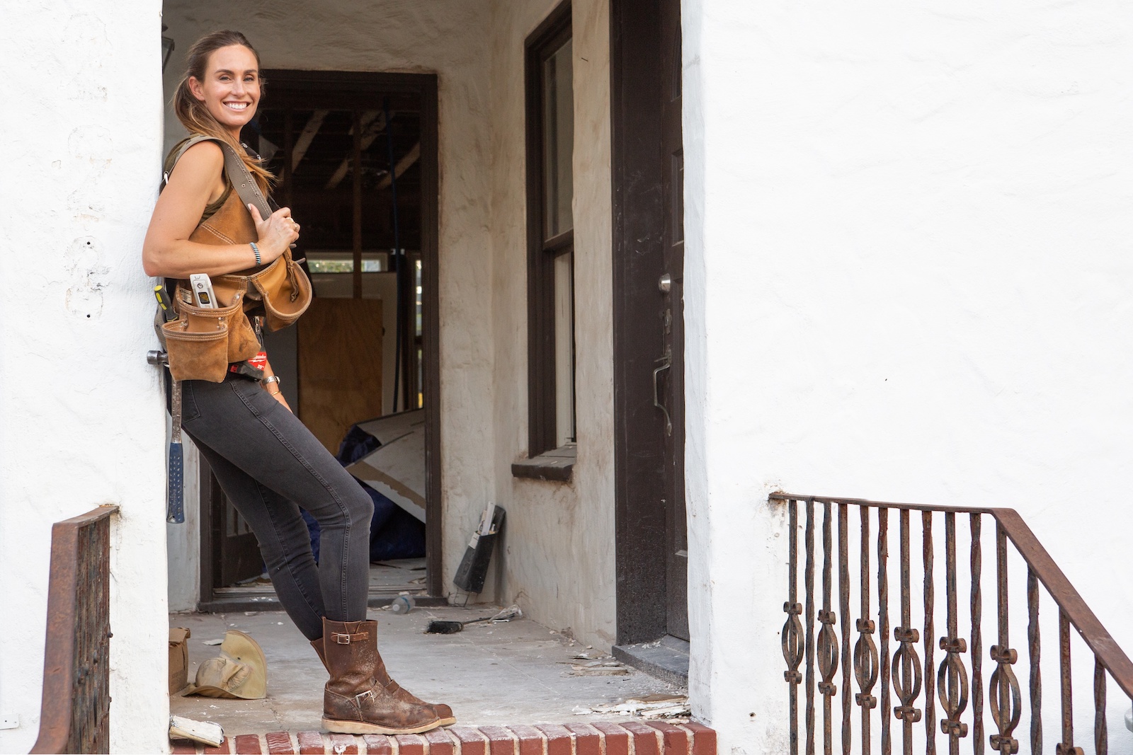 Kim Wolfe from HGTV's 'Why the Heck Did I Buy This House' smiles in a doorway with a toolbelt over her shoulder