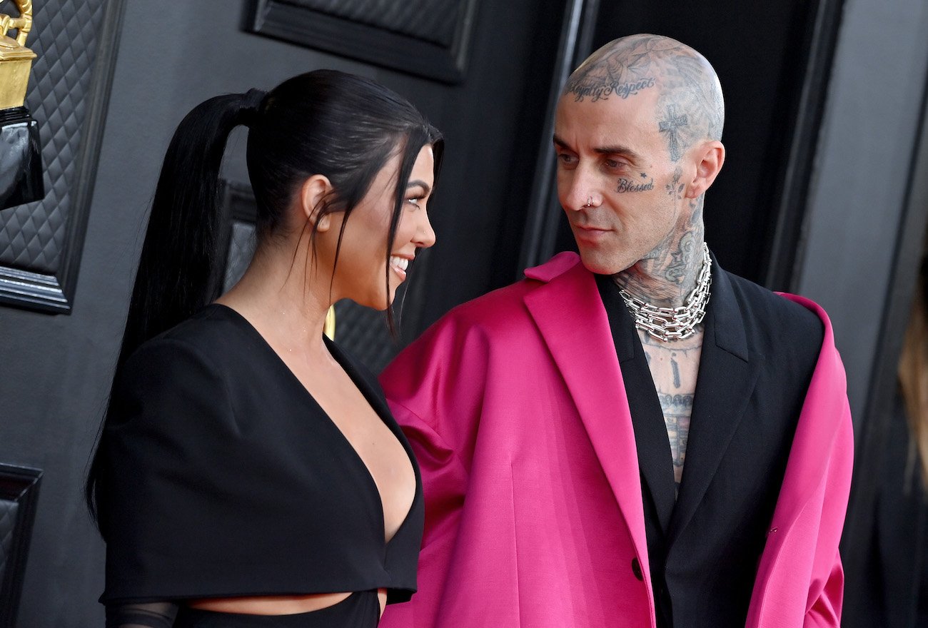 Kourtney Kardashian wearing a black outfit and looking at Travis Barker, who is wearing a pink coat