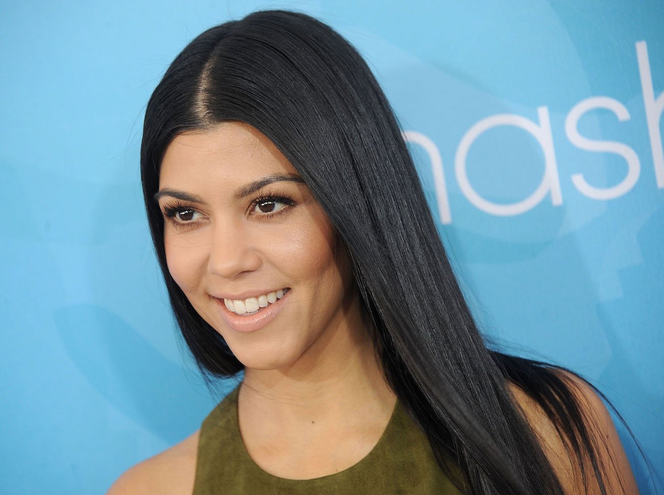 Kourtney Kardashian looking on while smiling and wearing a green outfit
