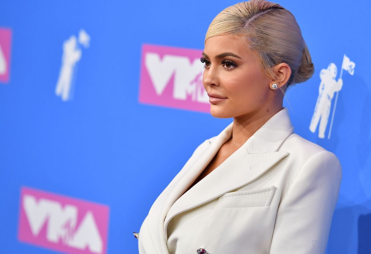 Kylie Jenner having blonde hair and wearing a white outfit while standing in front of a blue background