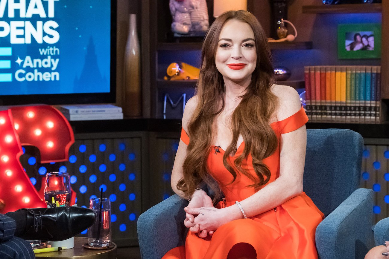 Lindsay Lohan wearing a red off-shoulder dress and sitting on a blue chair