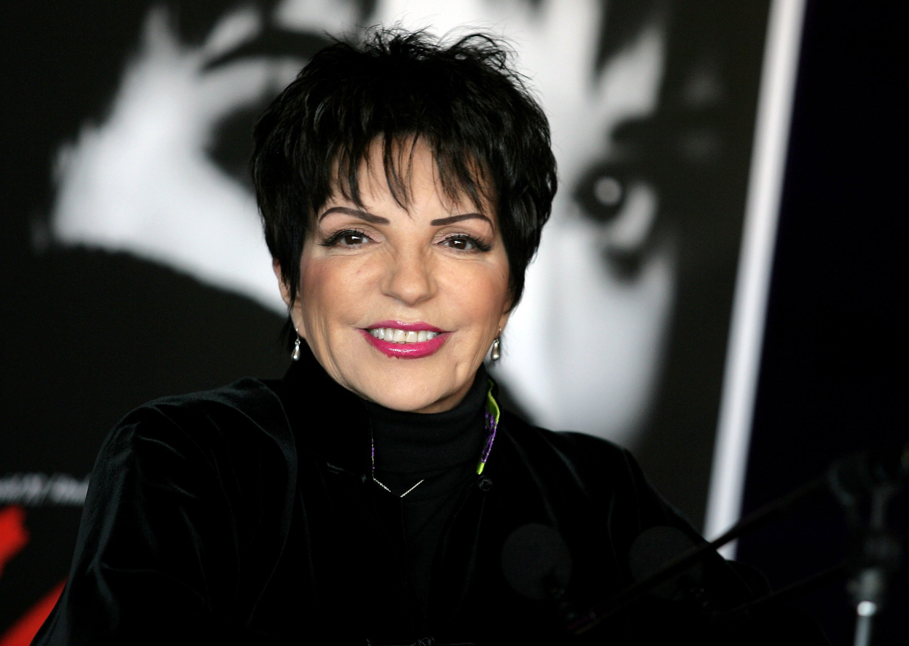Liza Minnelli wears a black turtleneck and stands in front of a black and white background.