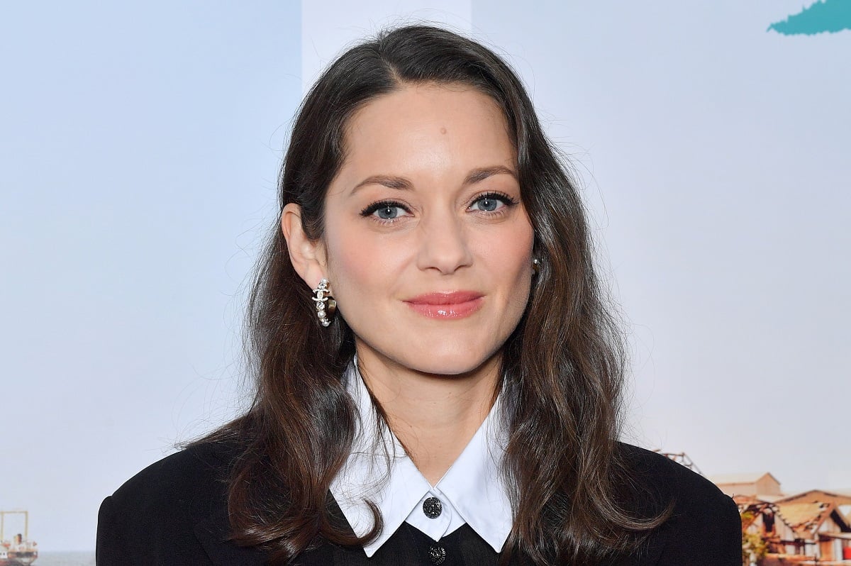 Marion Cotillard smirking while wearing a black sweater.