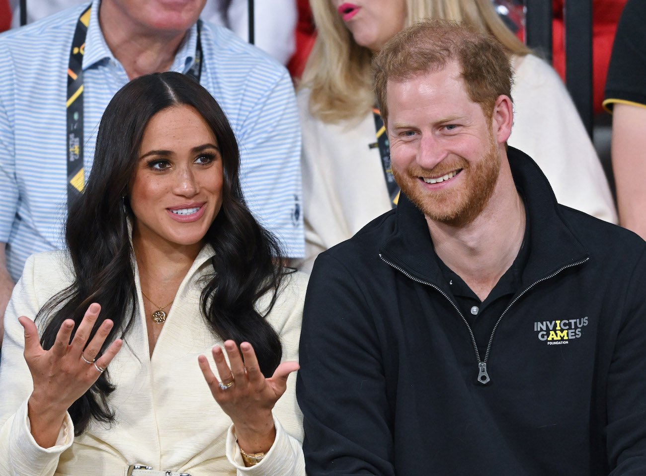 Meghan Markle wearing a white outfit and talking to Prince Harry, who is wearing a black outfit