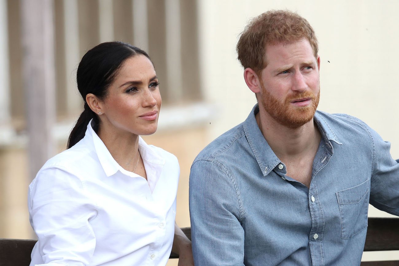 Meghan Markle wearing a white shirt and Prince Harry wearing a blue shirt, both looking to the right side of the photo
