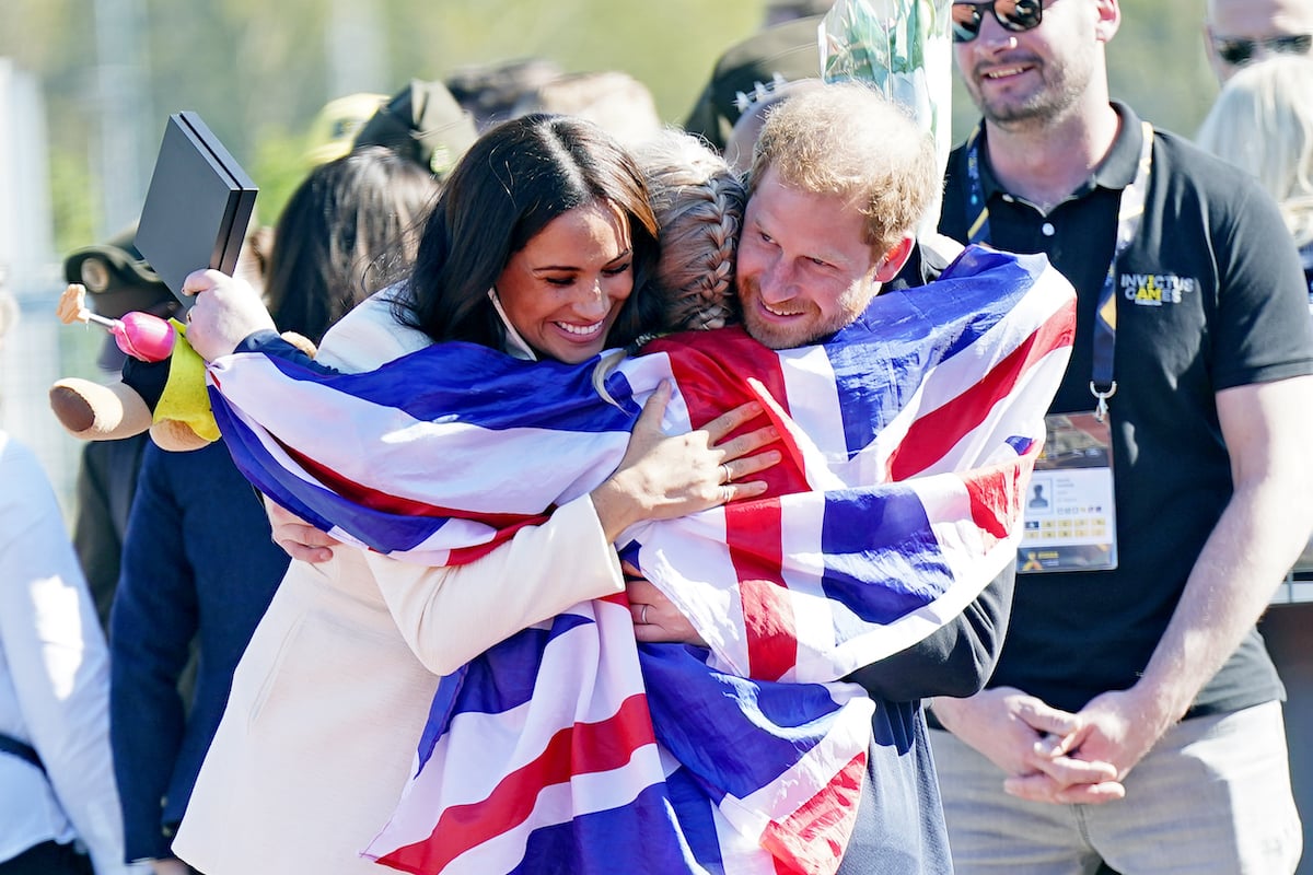 Meghan Markle and Prince Harry embrace Lisa Johnston she holds a British flag at the Invictus Games