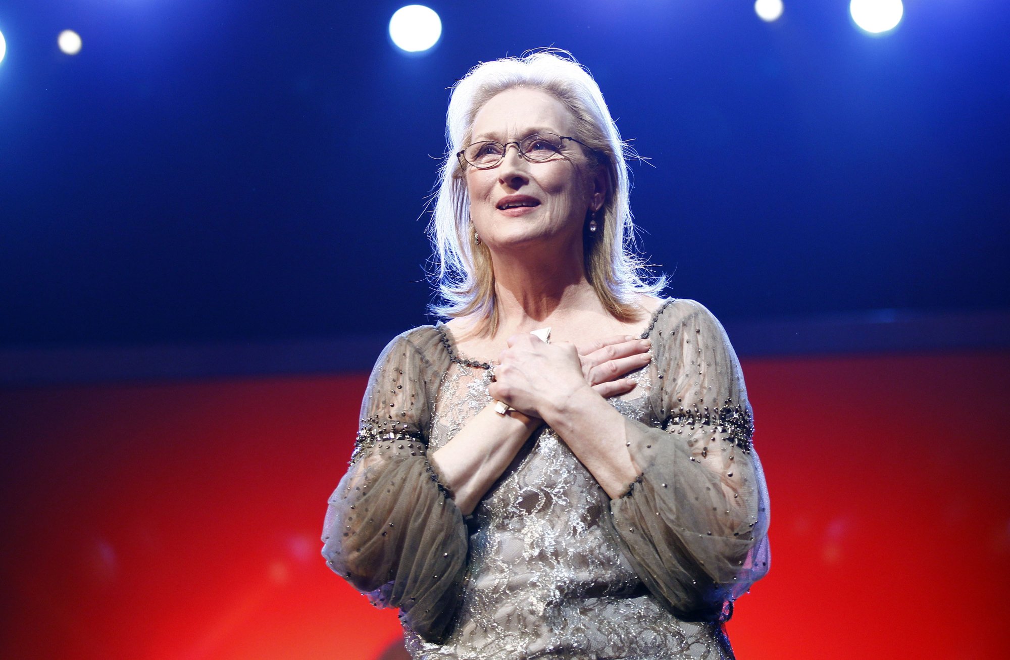 Meryl Streep being honored for her movies holding her hands over her chest wearing a silver and beaded gown
