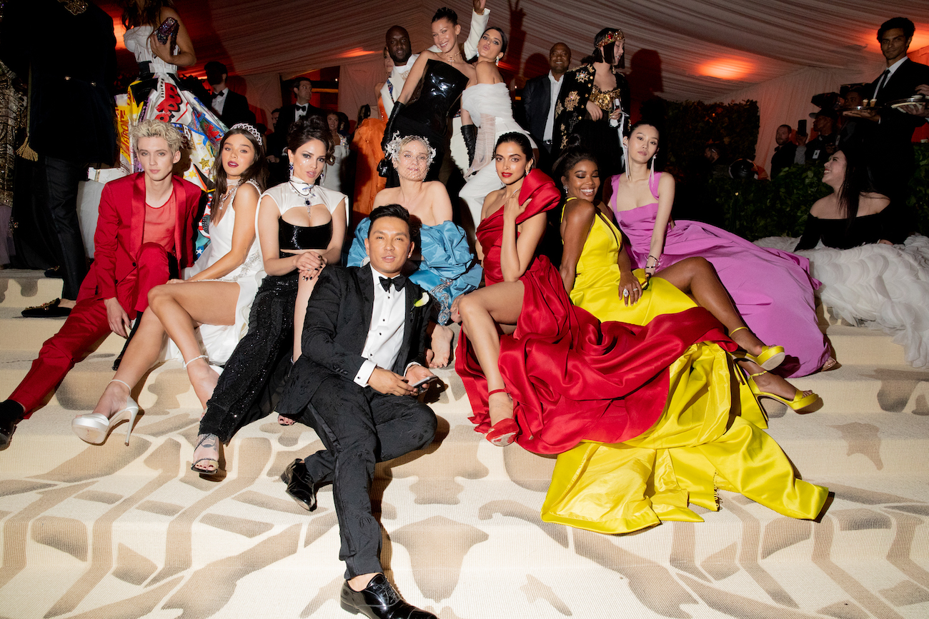 Attendees in colorful outfits sitting on the steps at the Met Gala 2018