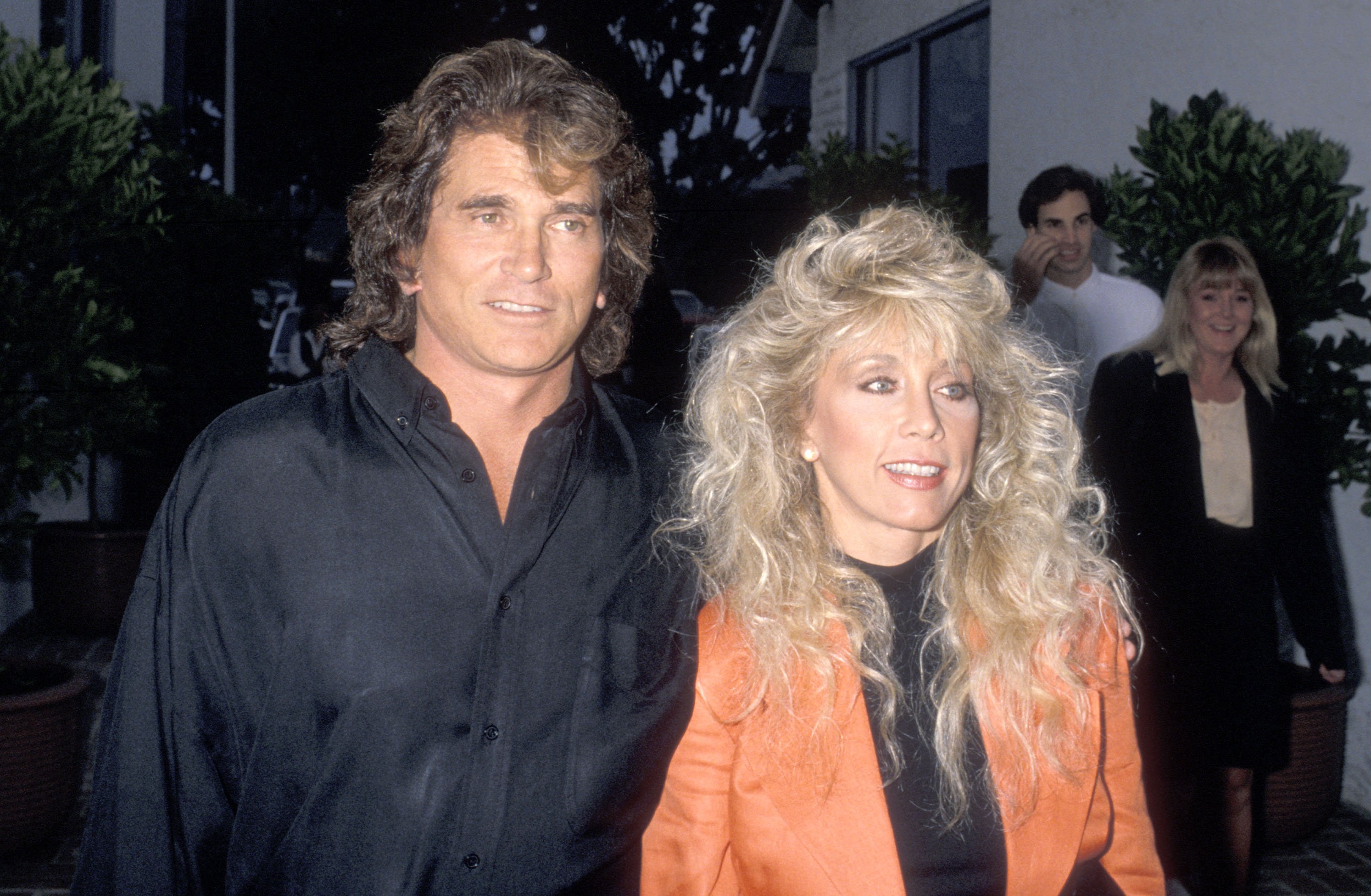 Michael Landon wears a black button down shirt and Cindy Landon wears an orange jacket as they attend a restaurant opening. 