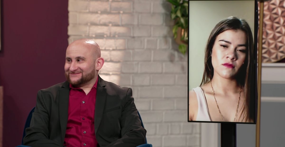 Mike wearing a red shirt and a suit jacket during the '90 Day Fiancé: Before the 90 Days' Season 5 tell-all, sitting next to Ximena who is on a screen.