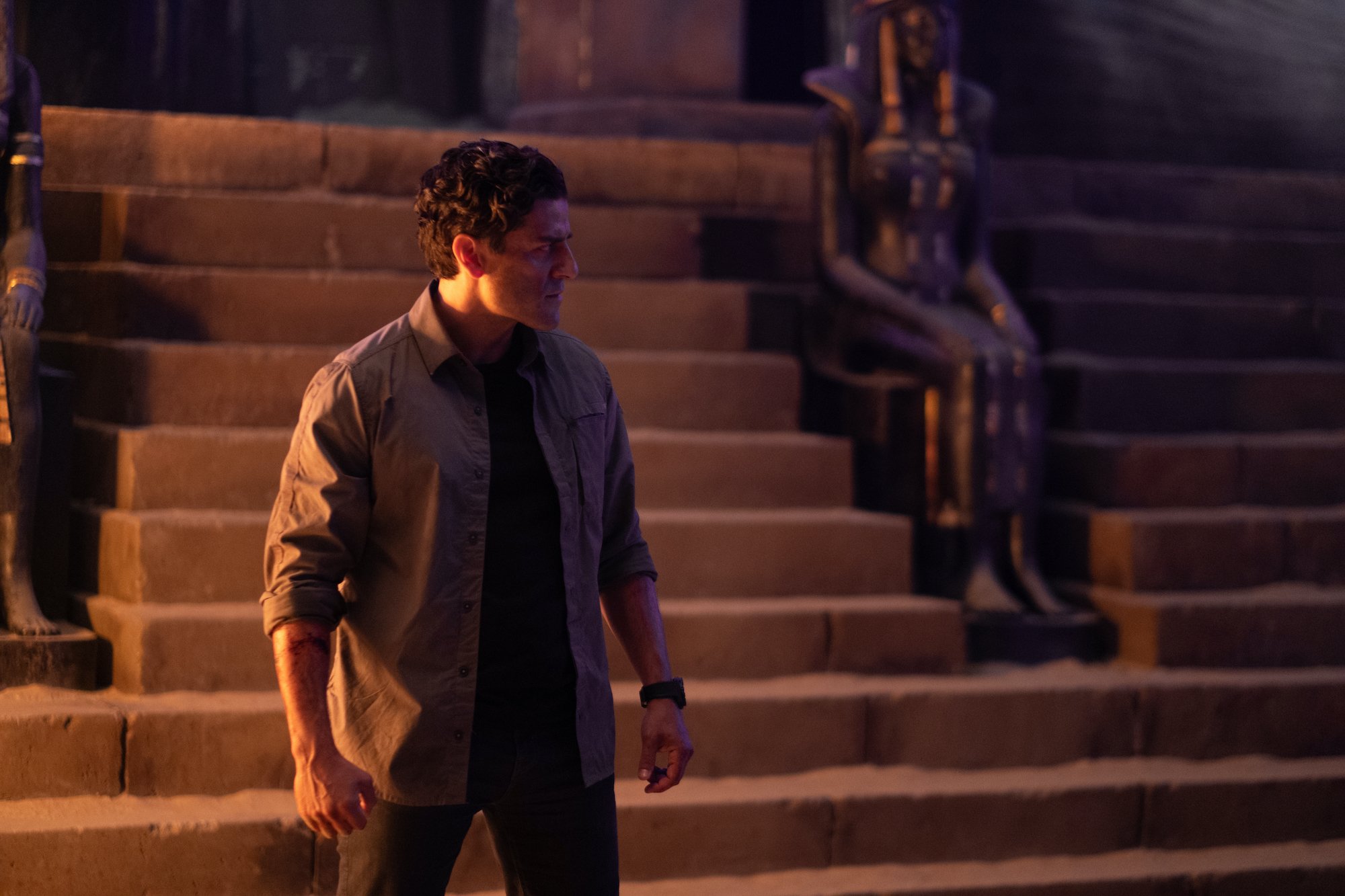'Moon Knight' Episode 4 star Oscar Isaac, in character as Marc Spector, wears a light gray unbuttoned long sleeve shirt over a black shirt and black pants.