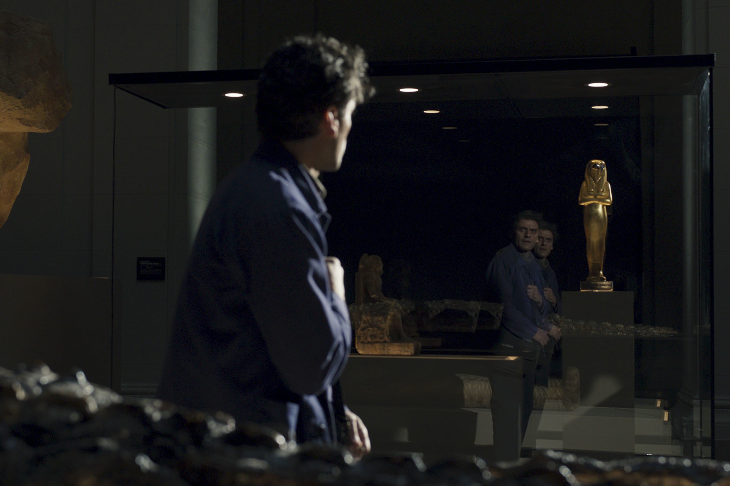 Oscar Isaac, who might appear as Jake Lockley in 'Moon Knight,' stars in a scene as Steven Grant and Marc Spector. Steven looks at his double reflection while wearing a blue jacket and gray pants.