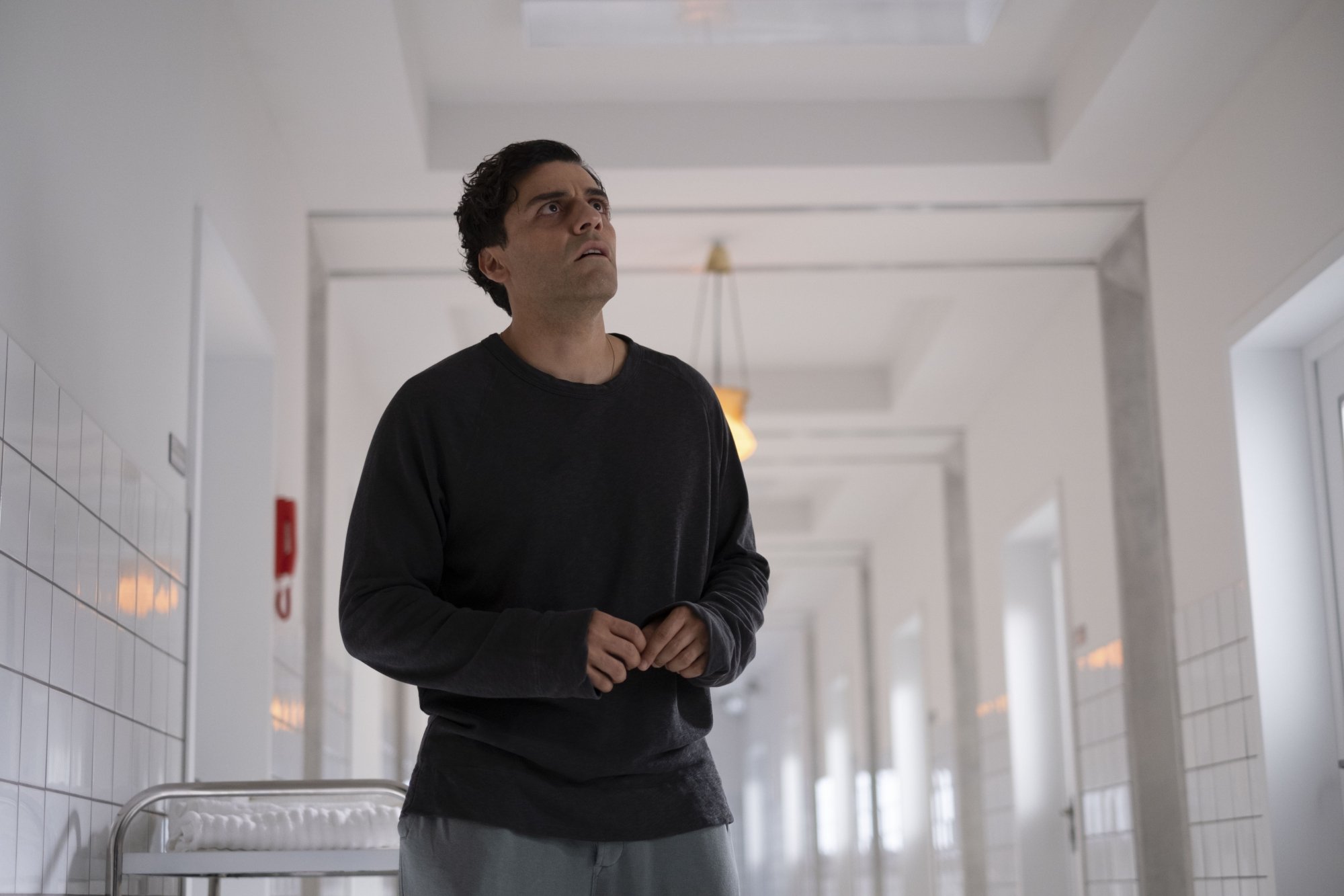 Oscar Isaac as Steven Grant in Moon Knight stands in a hospital hallway with ragged clothes.