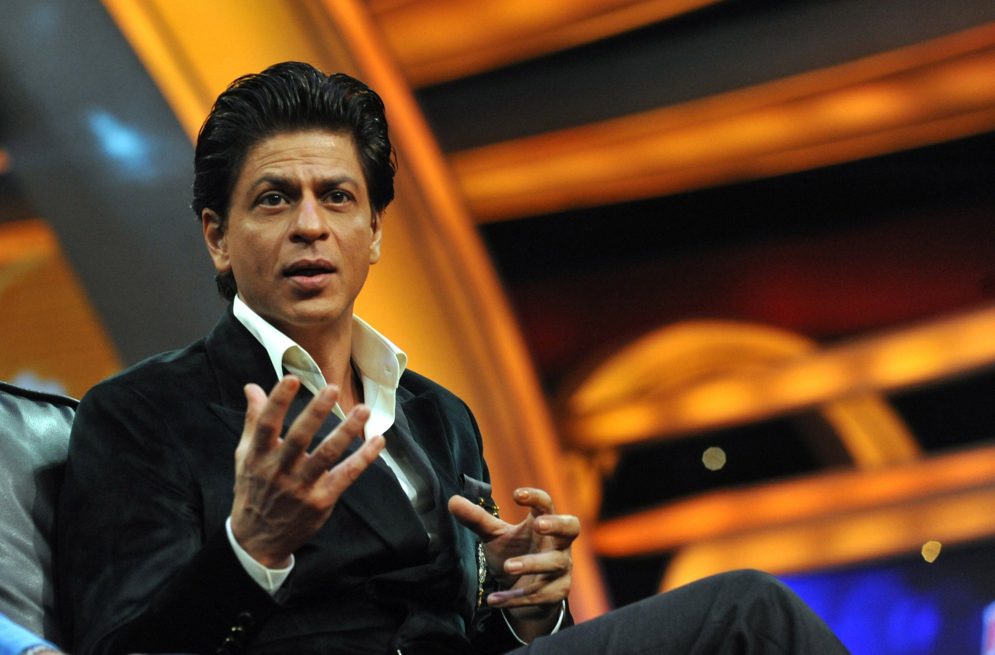 Movie actor Shah Rukh Khan wearing a suit and using his hands to talk