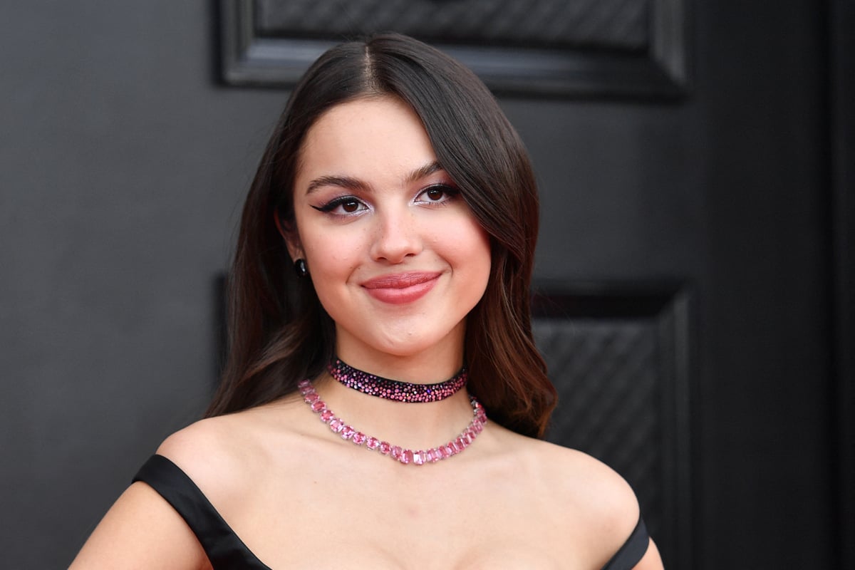 Wearing a black off the shoulder dress and pink choker necklace, Olivia Rodrigo poses on the red carpet of the 64th Annual Grammy Awards in Las Vegas, NV.