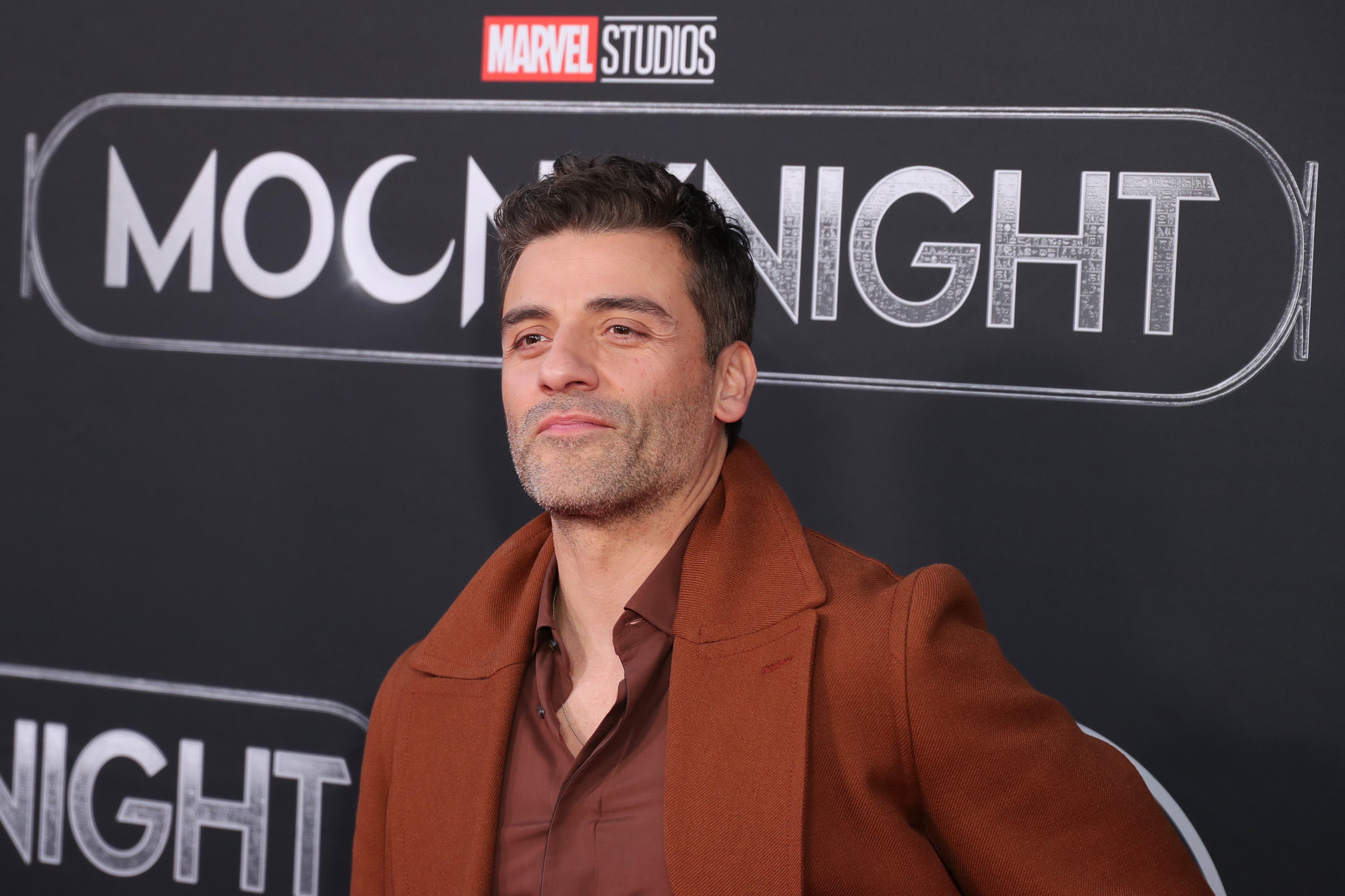 'Moon Knight' star Oscar Isaac wears a light brown coat over a maroon button-up shirt.