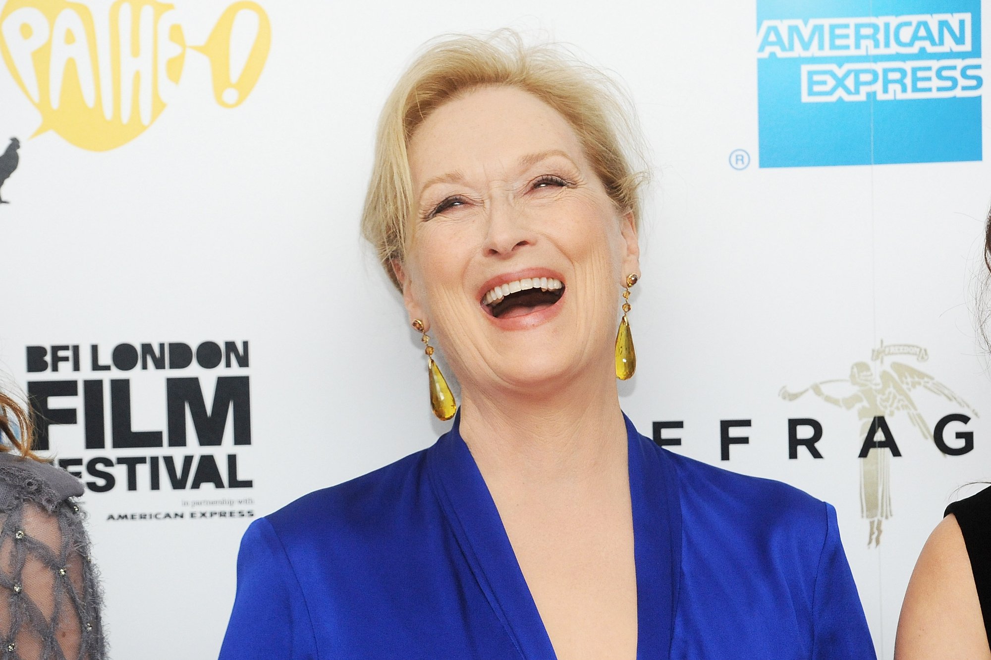 Oscar winner Meryl Streep wearing blue and laughing standing in front of a step and repeat