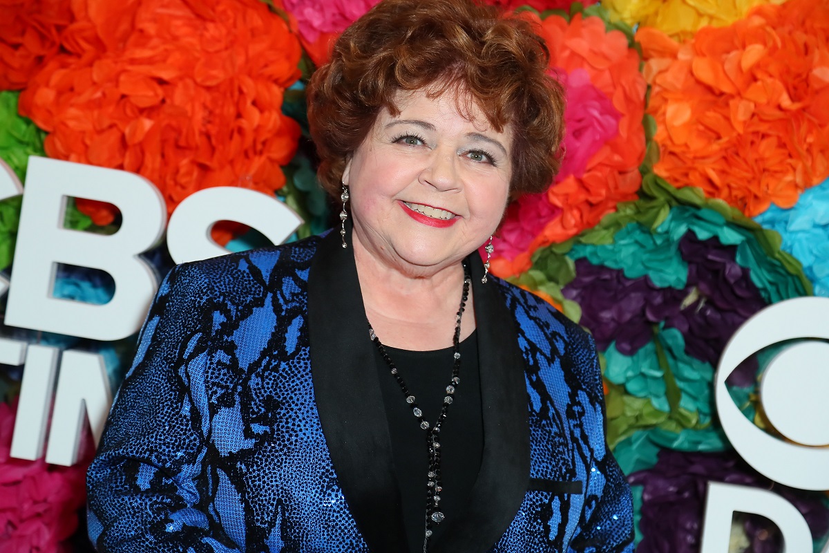 'Days of Our Lives' actor Patrika Darbo wearing a blue and black suit; and standing in front of a floral hedge.