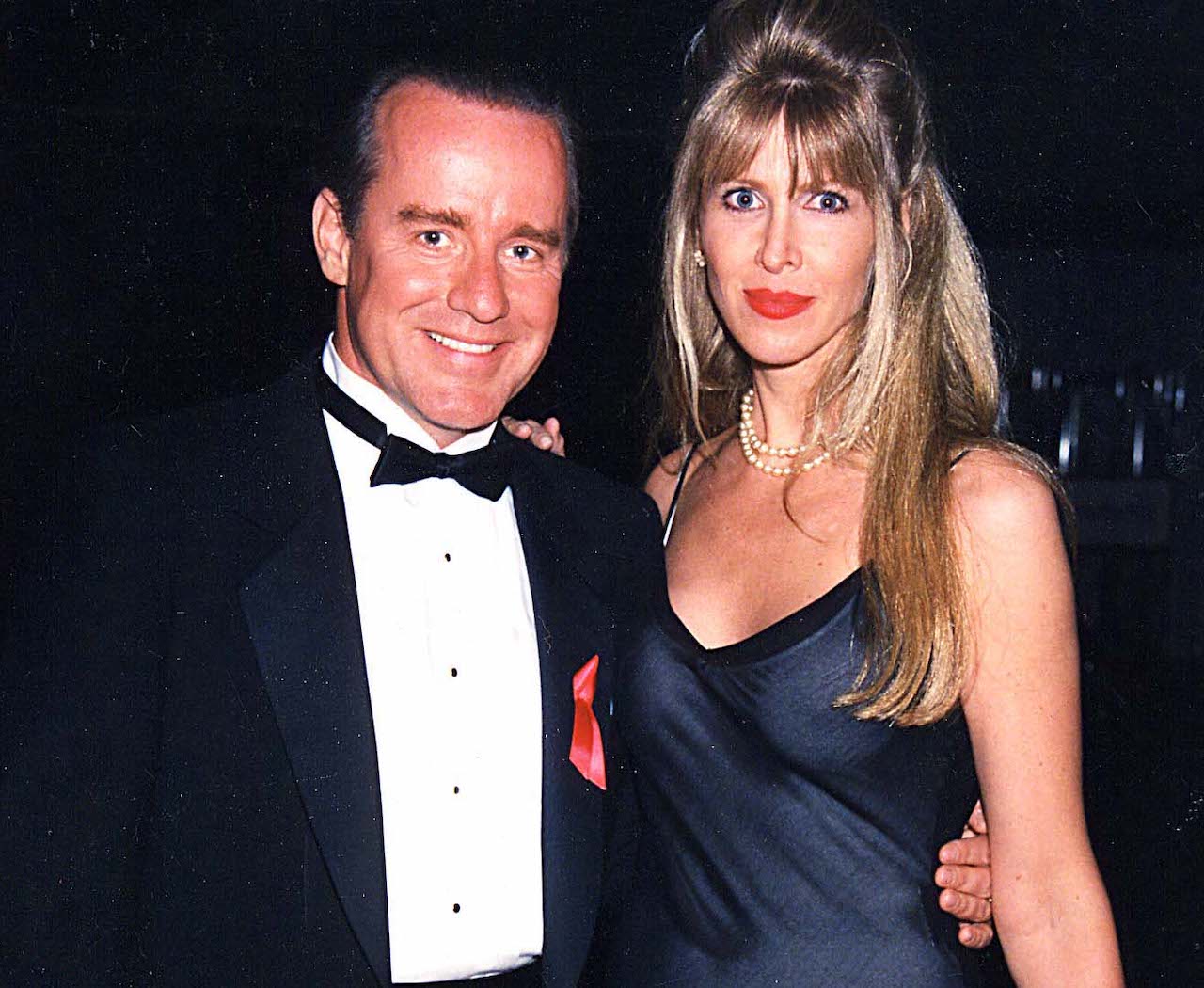 Phil Hartman in a tuxedo, standing with his wife, Brynn, in a black dress