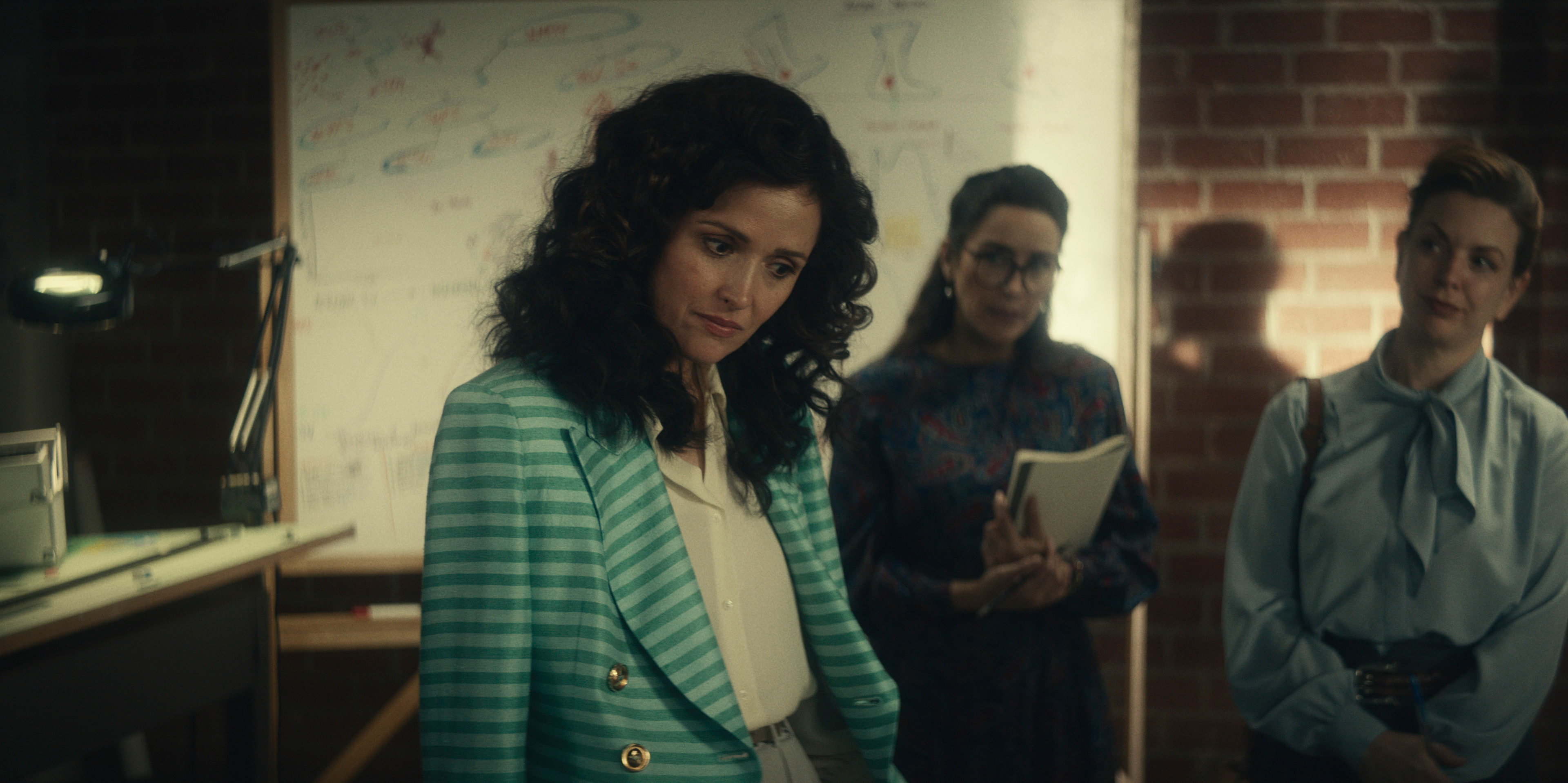 "Physical" star Rose Byrne wears an 80s style green striped jacket and looks concerned in a still from the show.