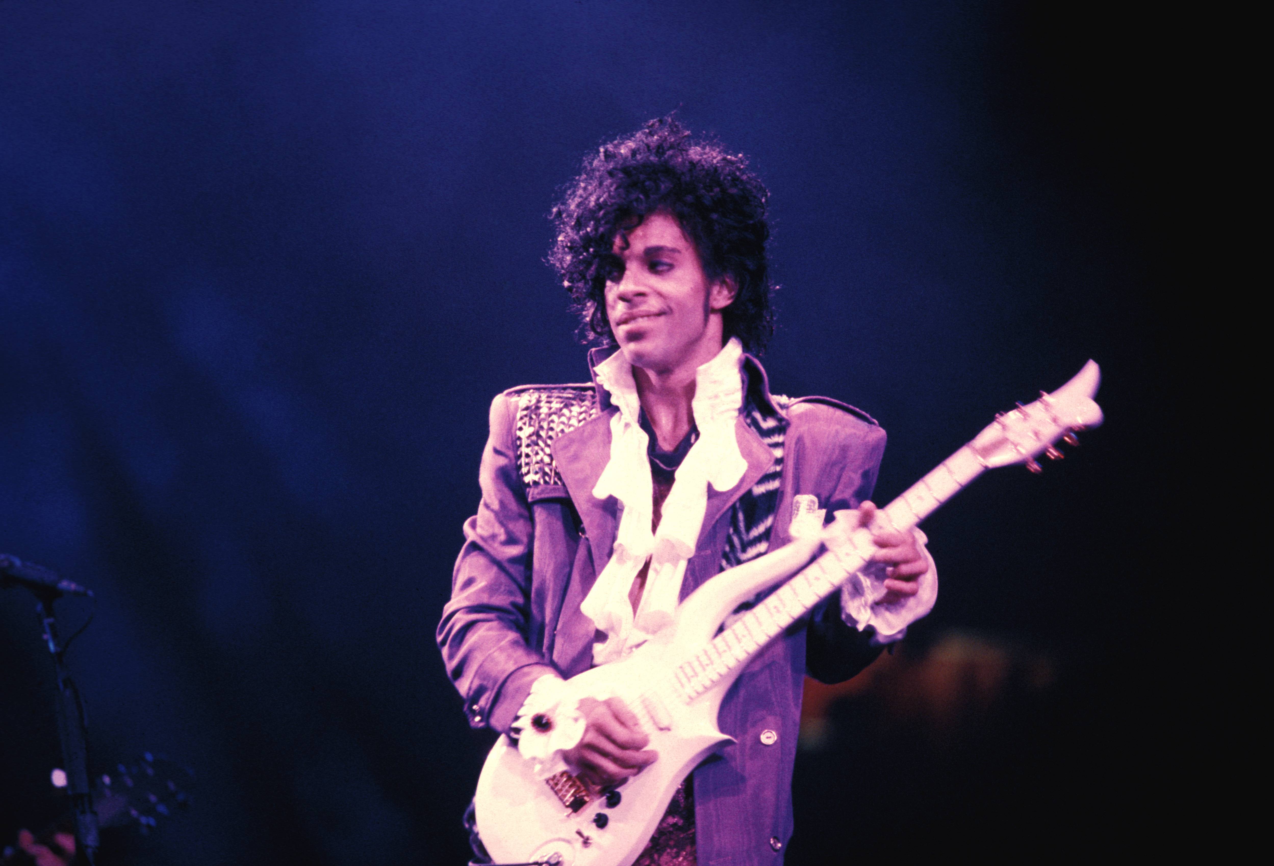 Prince smiles and holds a guitar during the Purple Rain tour.