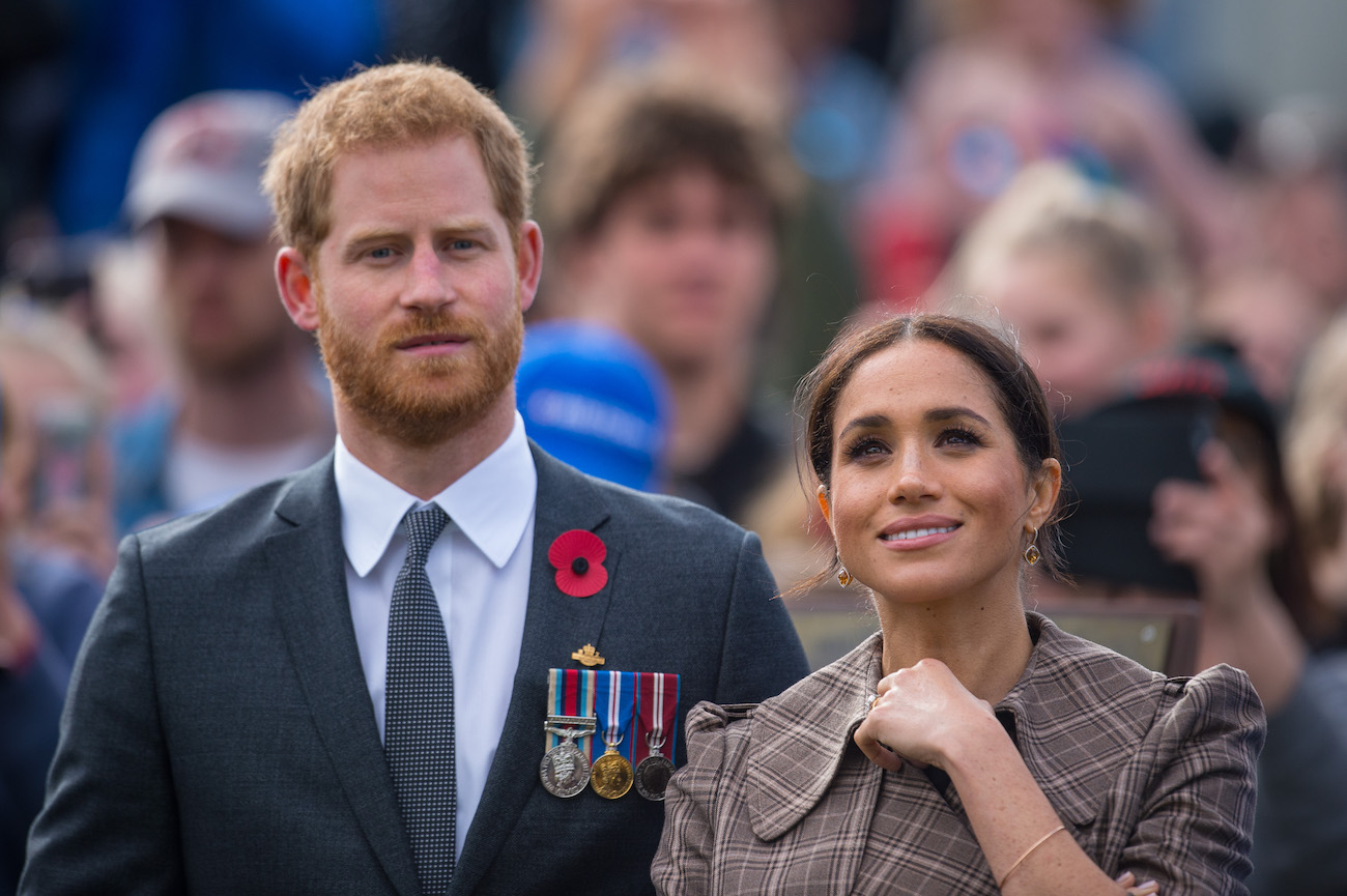 Prince Harry wearing a suit and standing next to Meghan Markle, who is wearing a brown outfit