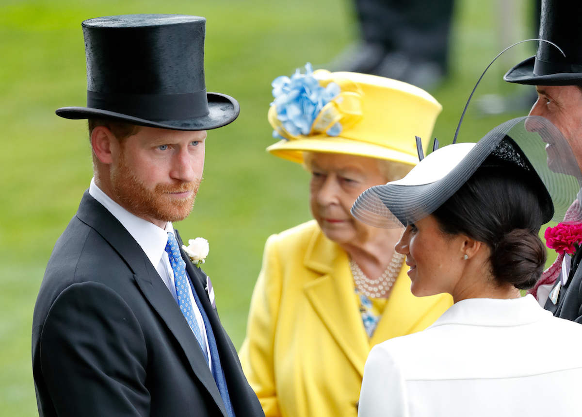 Prince Harry and Meghan Markle stand next to each other while Queen Elizabeth II stands in the background