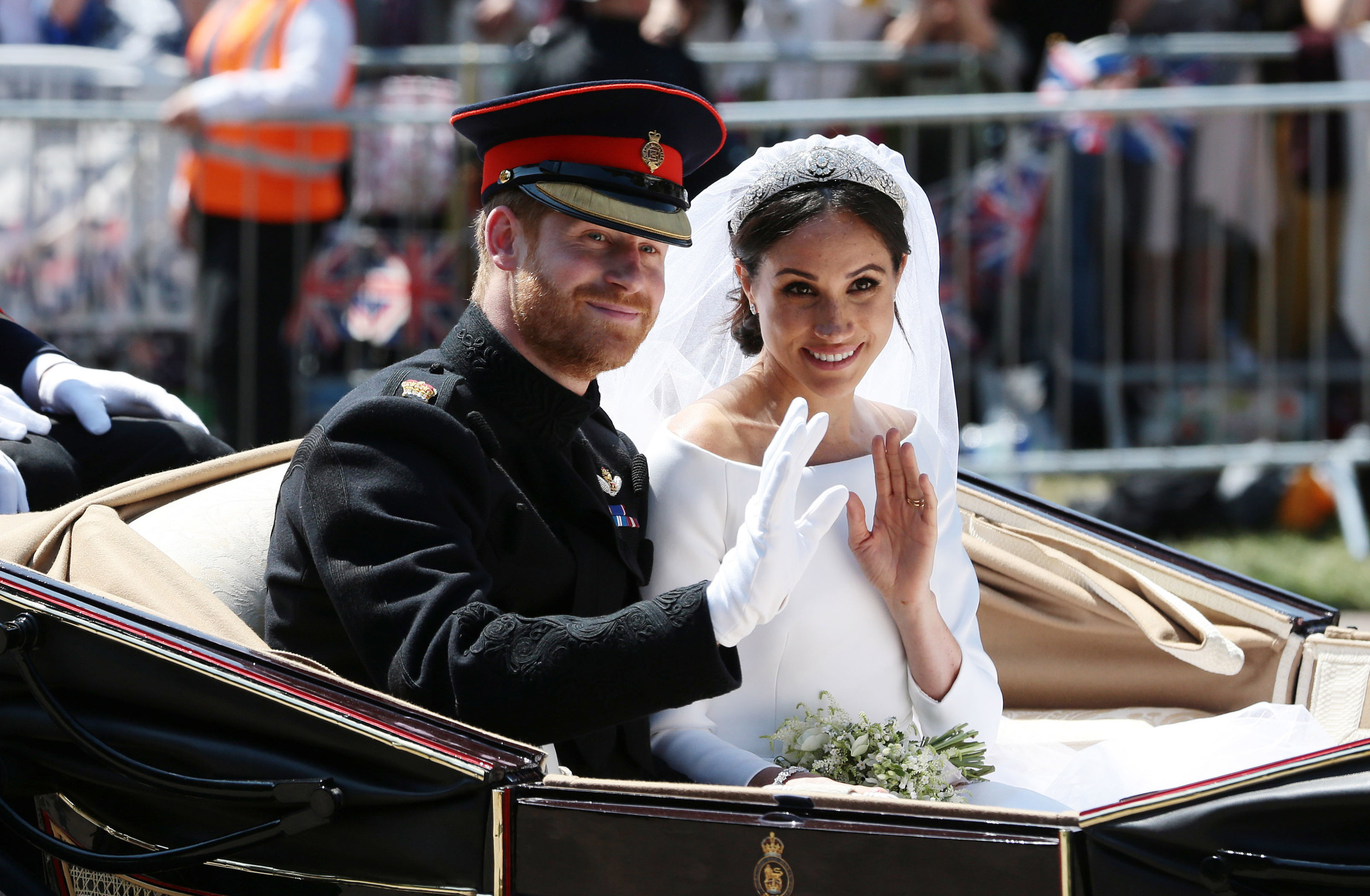 Prince Harry, who reportedly thought the best way to get Meghan Markle protection was through marriage, waves to the crowd with his wife during the carriage procession following their wedding