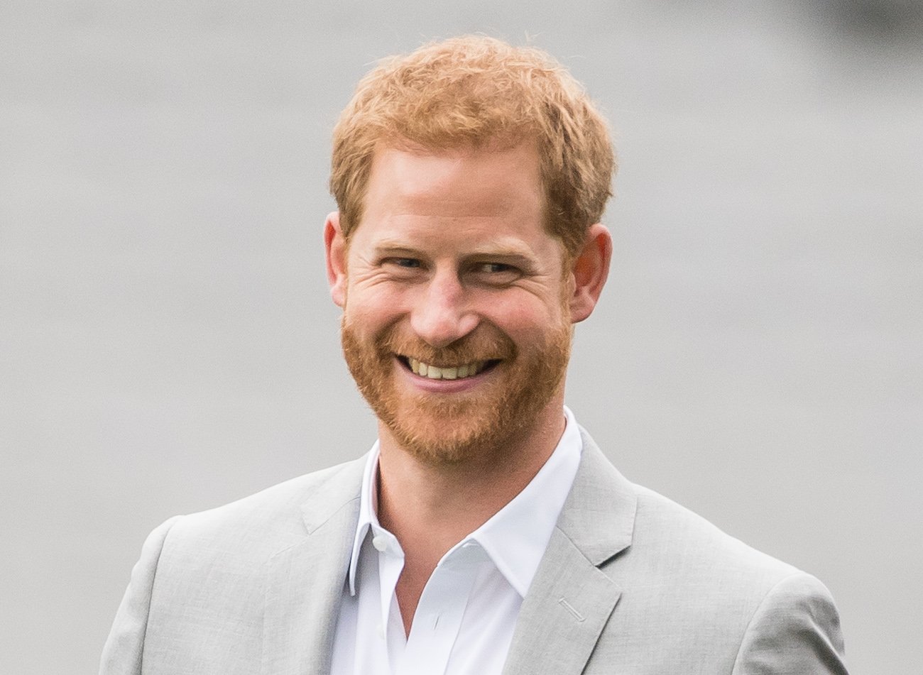 Prince Harry smiling while wearing a gray suit