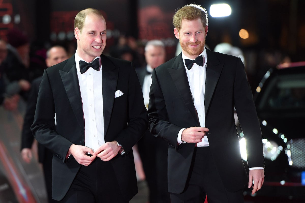 Prince William and Prince Harry smile as they walk next to each other wearing tuxedos