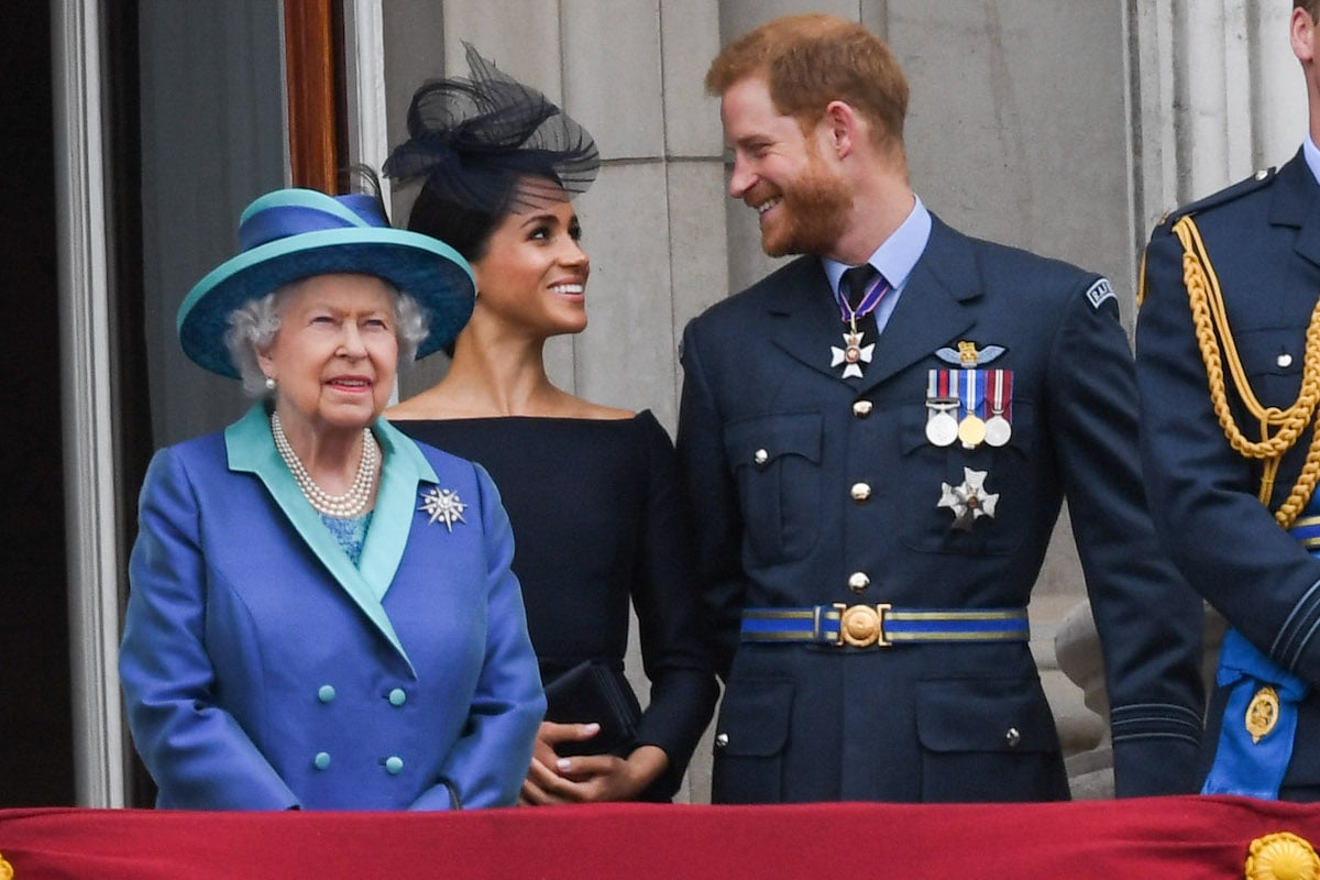 Prince Harry and Meghan Markle smile as they stand behind Queen Elizabeth II