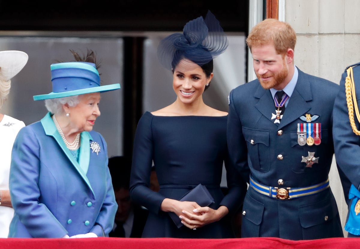Queen Elizabeth II, Meghan Markle, and Prince Harry stand on the balcony of Buckingham Palace wearing blue