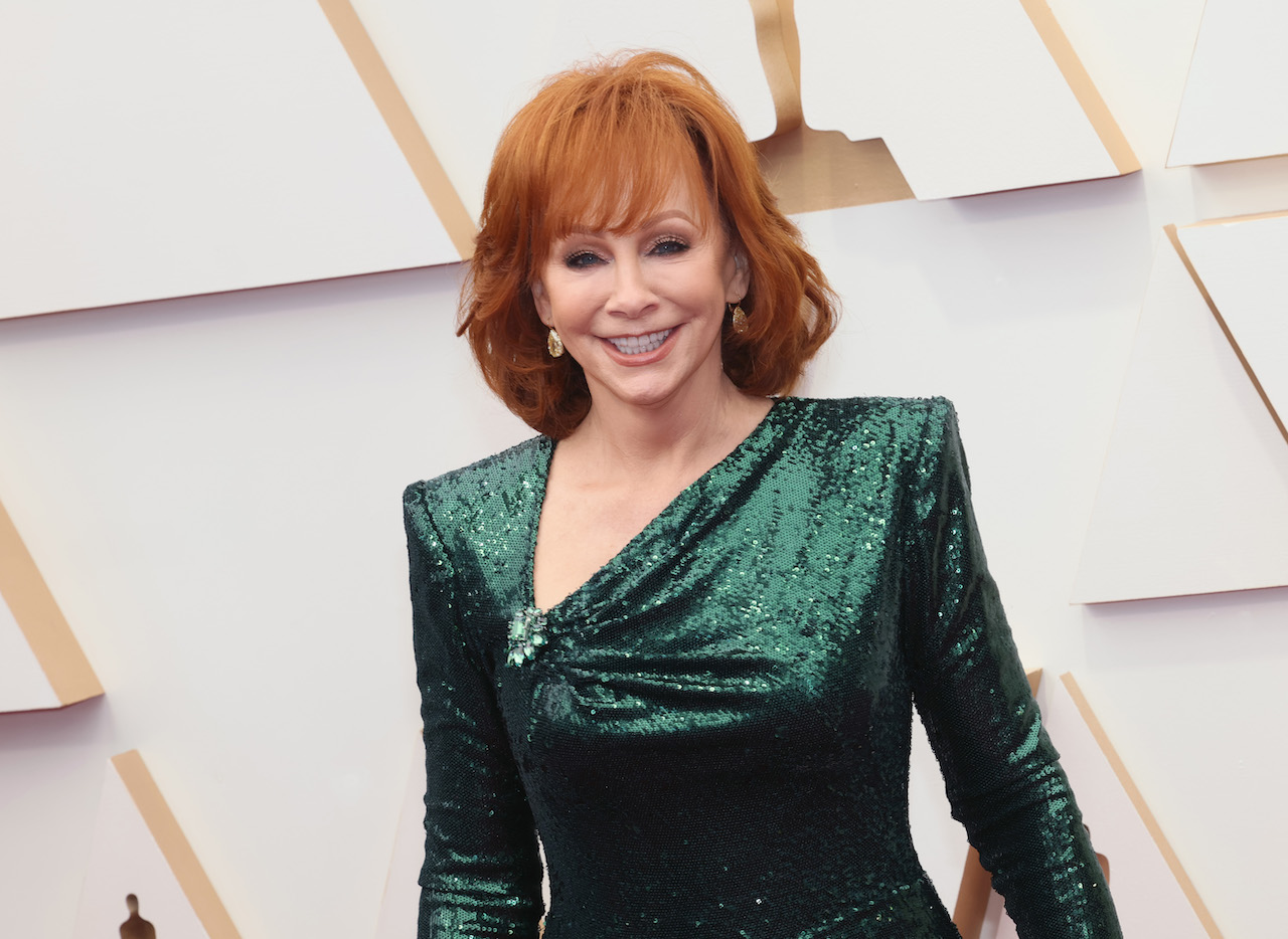 Reba McEntire in a sparkly, dark green dress, smiling for a picture at the the 94th Annual Academy Awards