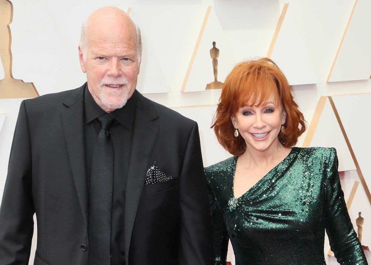 Rex Linn in a black suit and Reba McEntire in a dark green gown, posing and smiling for a picture in 2022