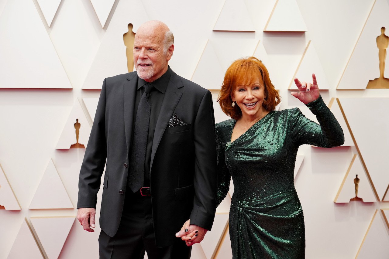 Rex Linn in a black suit, holding hands with Reba McEntire in a dark green dress