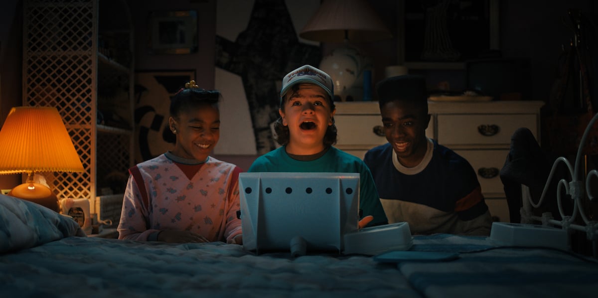 'Stranger Things 4' production still with Priah Ferguson as Erica Sinclair, Gaten Matarazzo as Dustin Henderson and Caleb McLaughlin as Lucas Sinclair looking at a Lite Brite on a bed. Stranger Things 4 clues