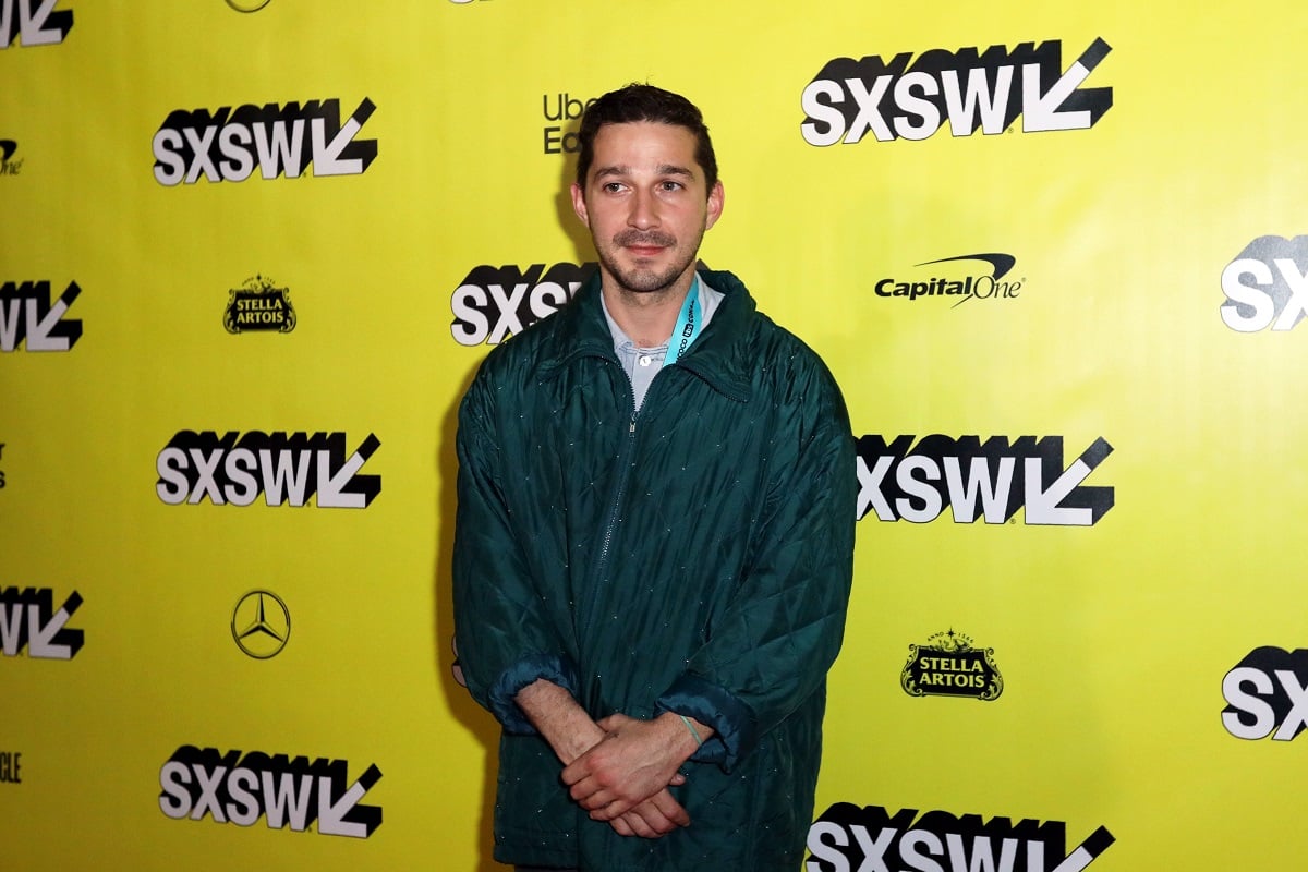 Shia LaBeouf smirking while wearing a jacket.