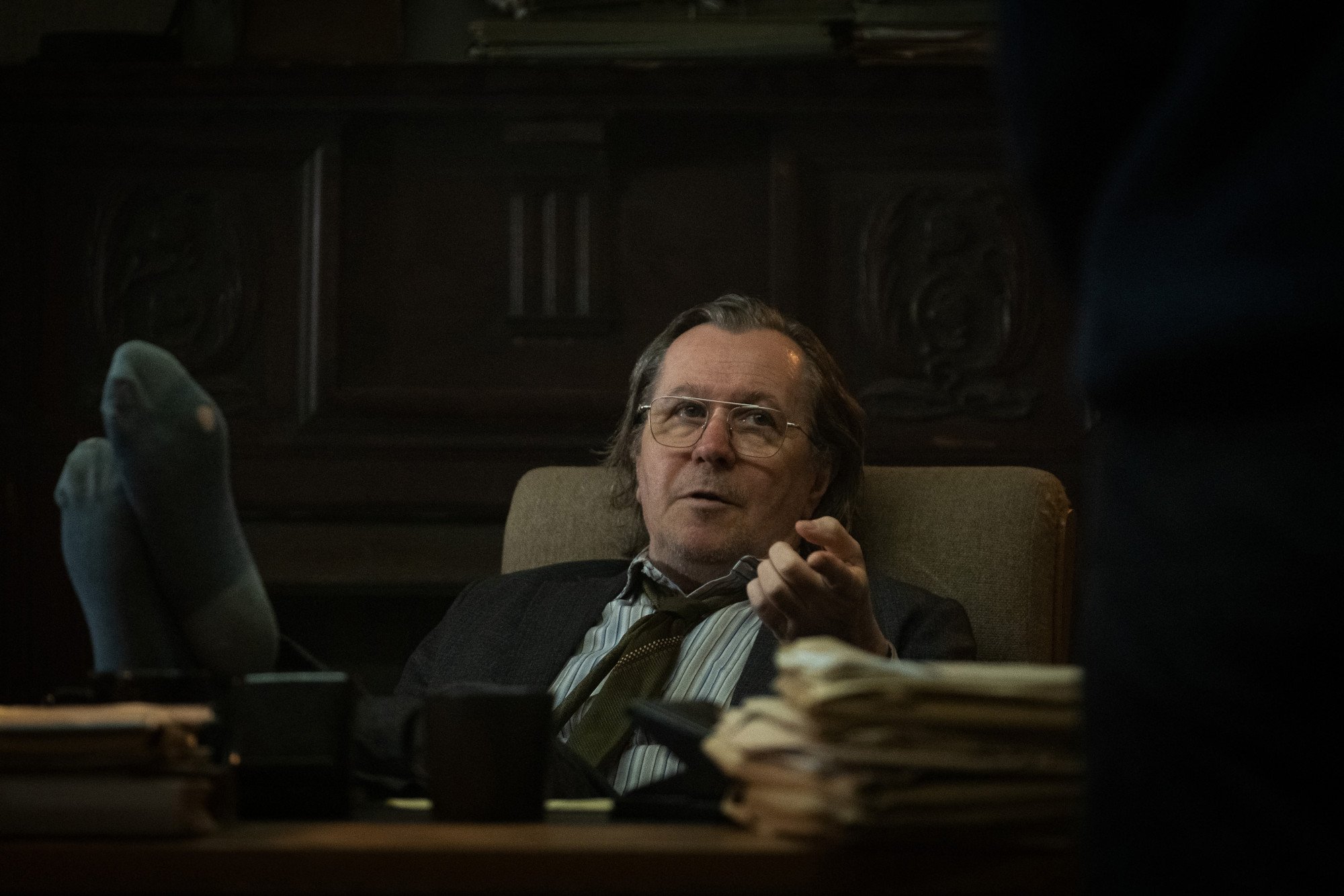 Gary Oldman as Jackson Lamb in Apple TV+'s new show 'Slow Horses.' He's sitting at his desk, and his feet are on top of it.