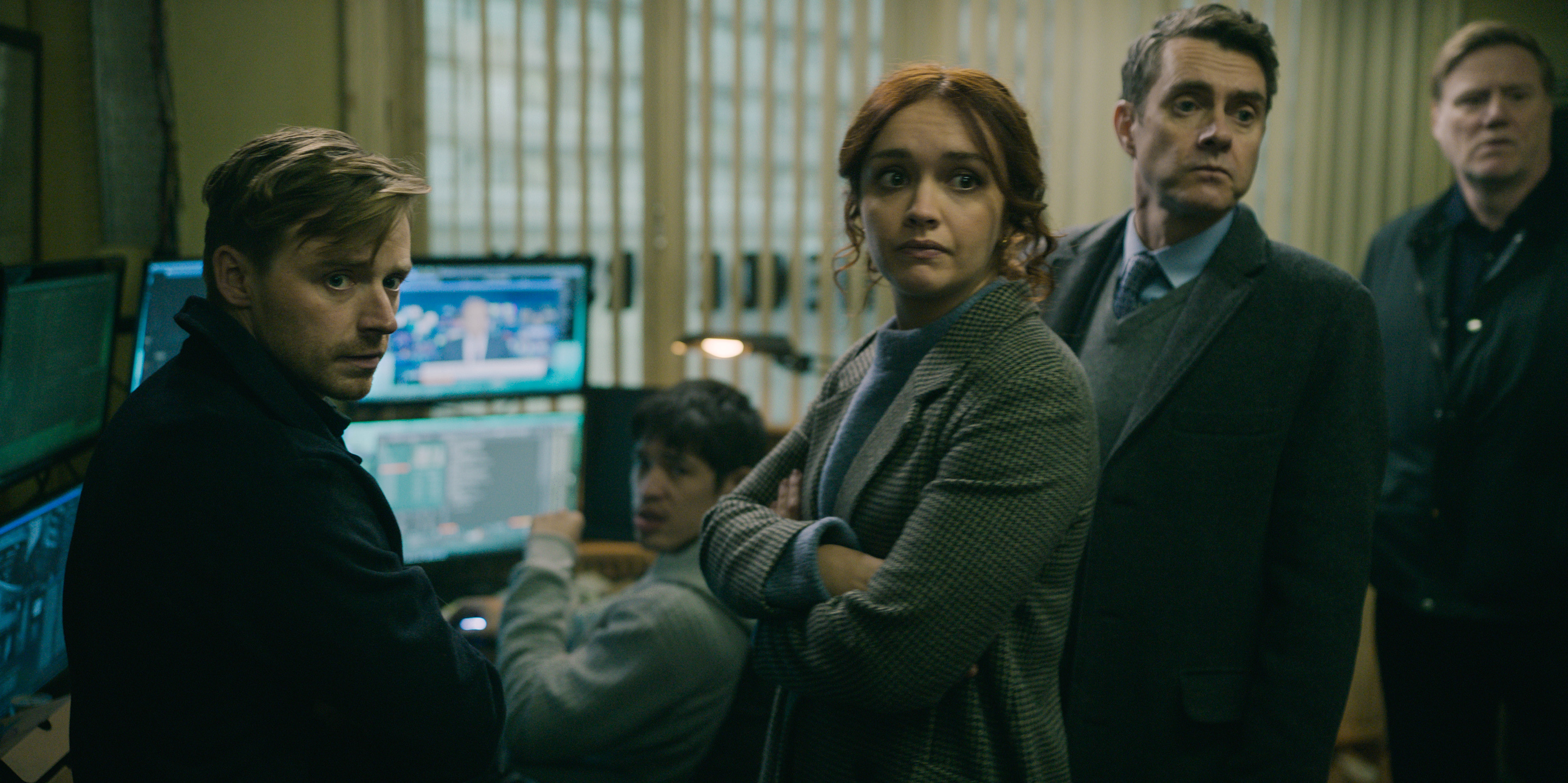 Jack Lowden, Christopher Chung, Olivia Cooke and Paul Higgins in an episode of 'Slow Horses' on Apple TV+. They're gathered around a computer and looking at someone facing away from it.