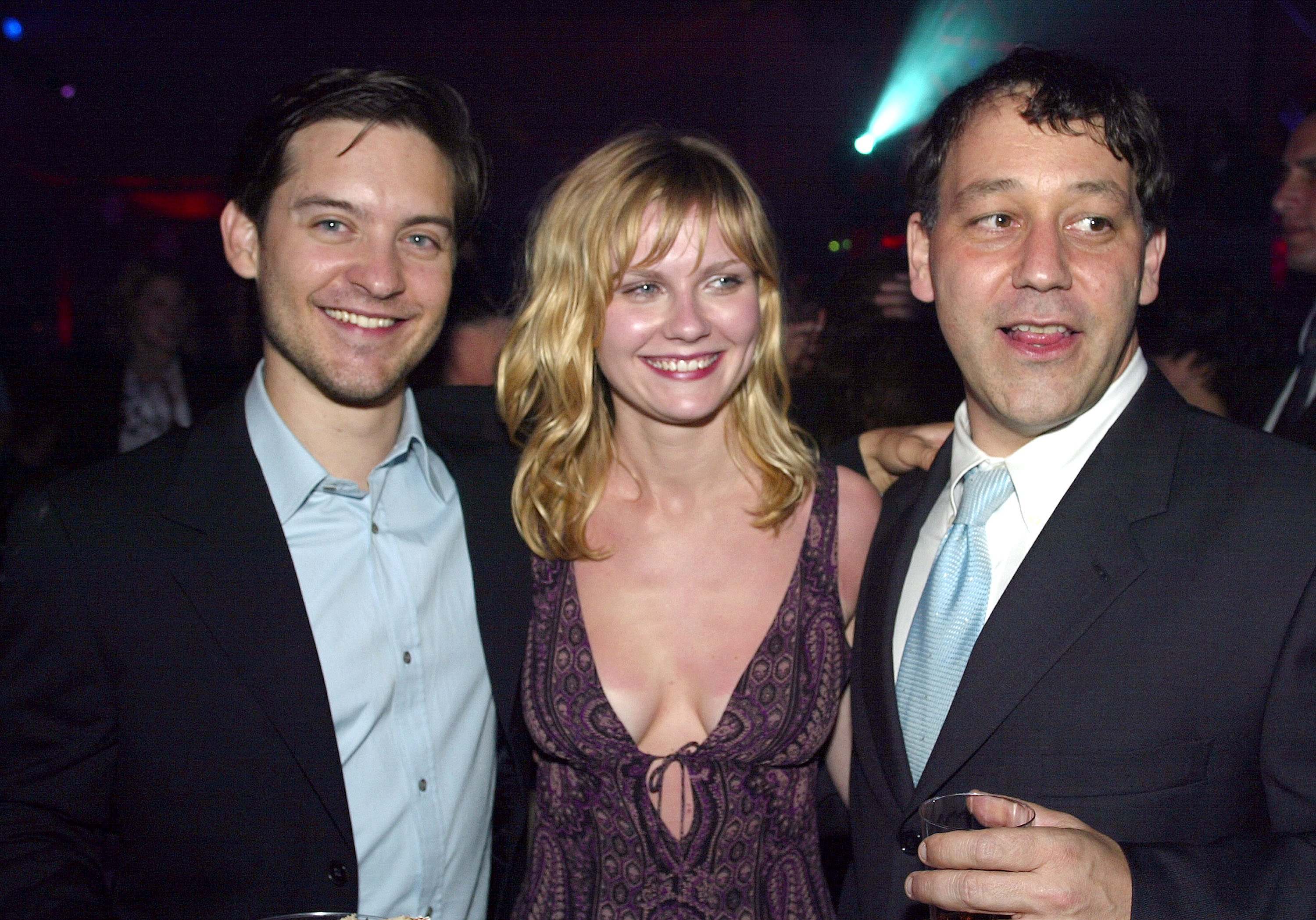 Tobey Maguire, Kirsten Dunst, and Sam Raimi, who fans want to see reunite for 'Spider-Man 4,' pose for a picture together. Maguire wears a black suit over a light blue button-up shirt. Dunst wears a purple paisley tank top. Raimi wears a black suit over a white button-up shirt and light blue tie.