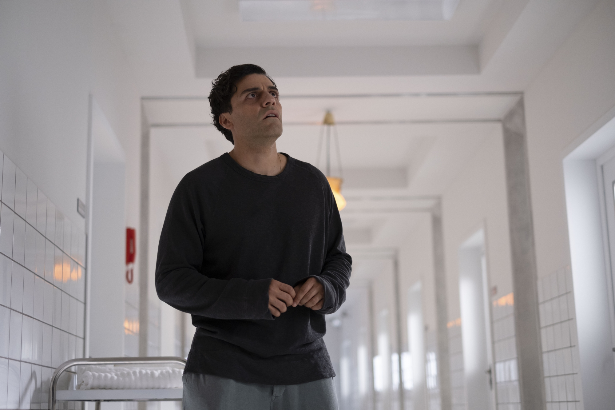 Oscar Isaac as Steven Grant in 'Moon Knight' Episode 5, which sets up the finale. He's wearing a black shirt and standing in an all-white hallway.