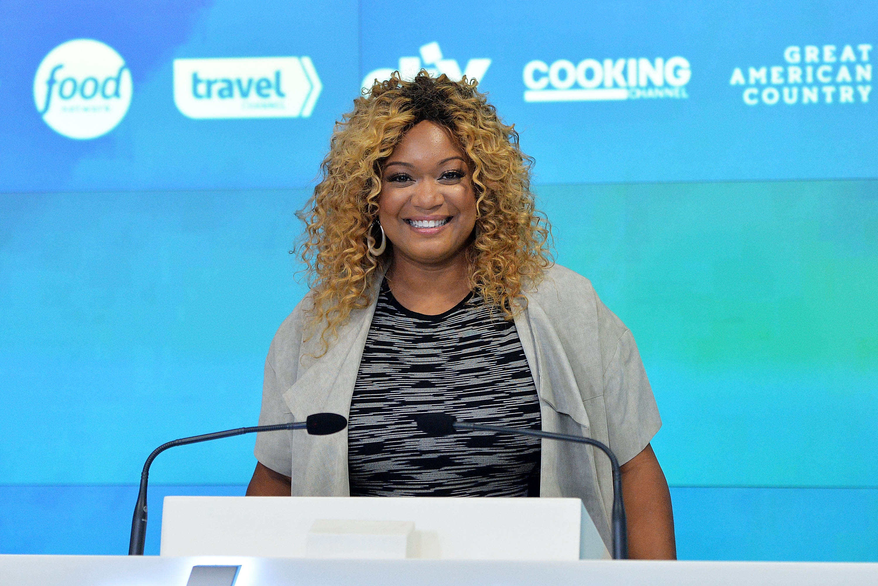 Food Network personality Sunny Anderson wears a short-sleeved gray sweater in this photograph.