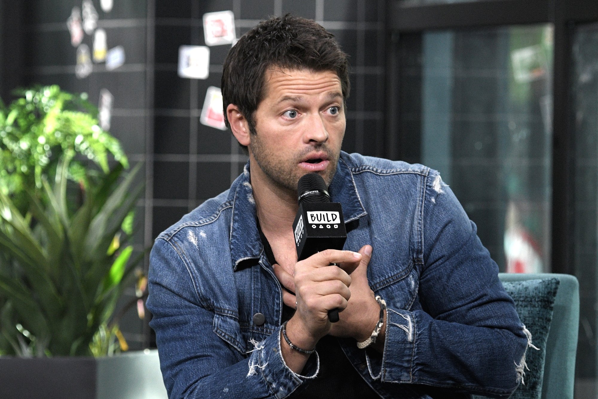 'Supernatural' star Misha Collins, who mistakenly came out as bisexual holding a microphone holding his hand over his chest wearing a jean jacket