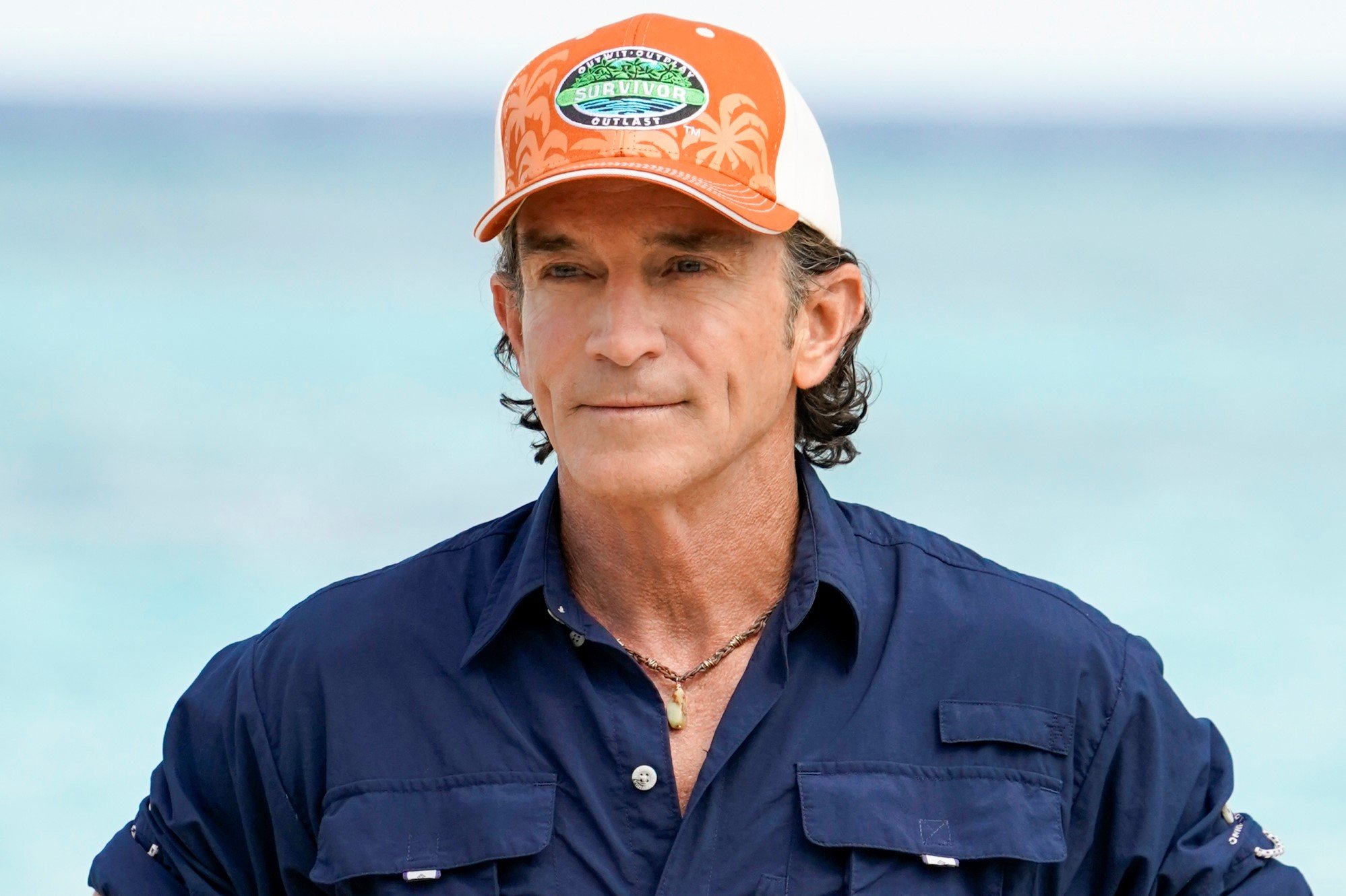 'Survivor' Season 42 host Jeff Probst wears a dark blue button-up shirt and orange 'Survivor' baseball hat.