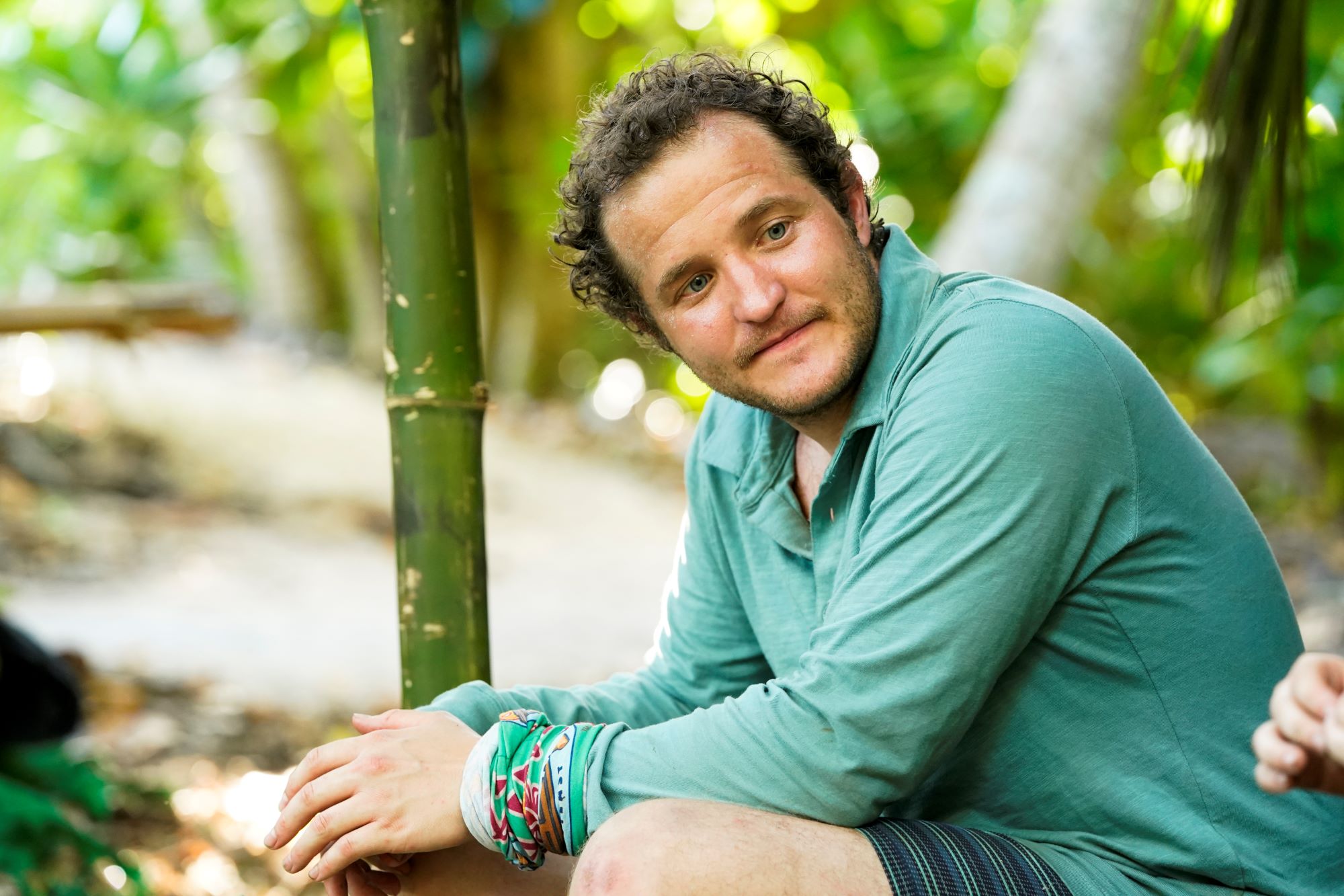 'Survivor' Season 42 castaway Daniel Strunk wears a green long-sleeved button-up shirt, green and black striped shorts, and his green buff around his wrist.