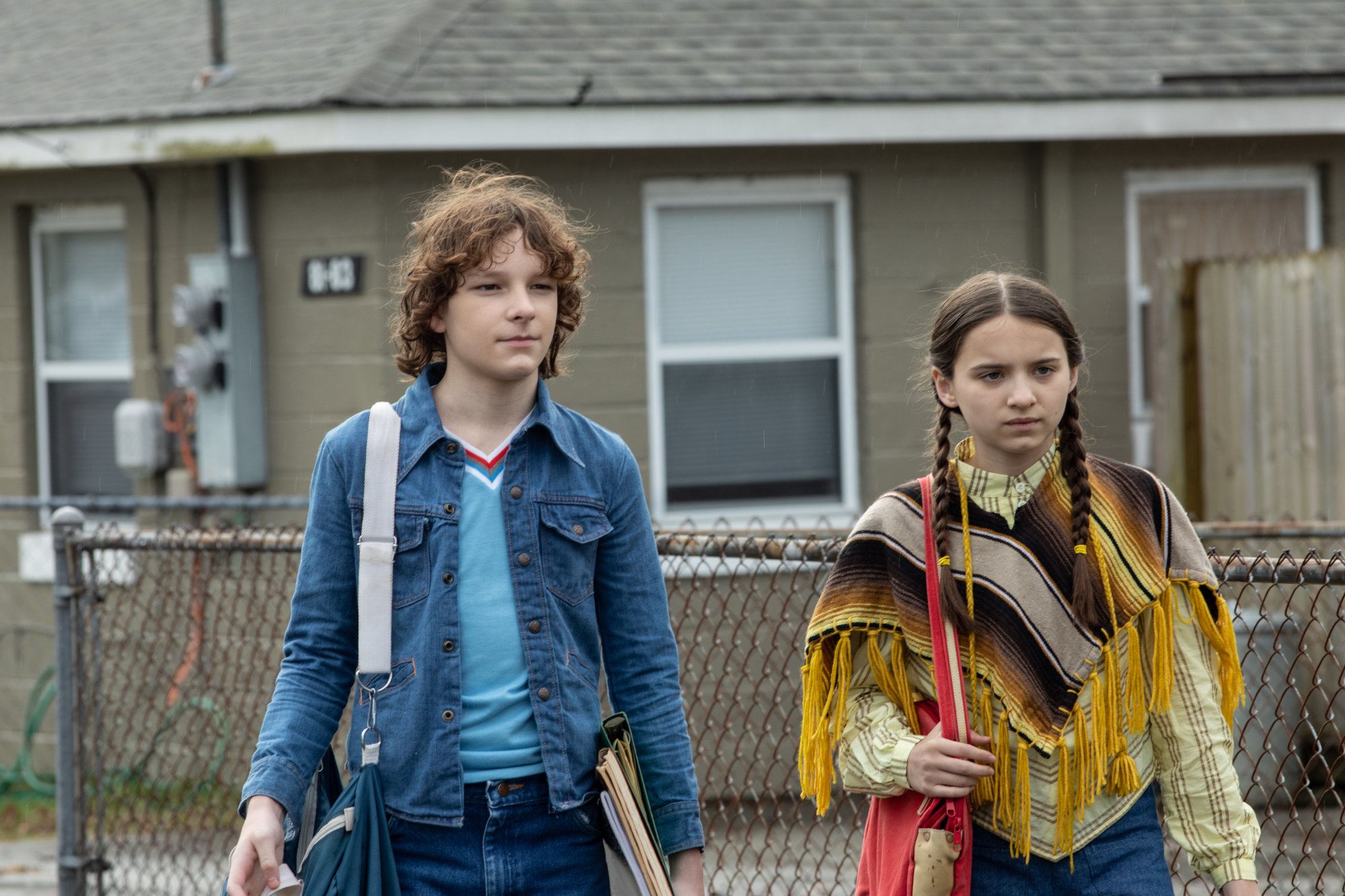 'The Black Phone' Mason Thames as Finney Shaw and Madeleine McGraw as Gwen Shaw holding their bags on their shoulders in front of a house in suburbia