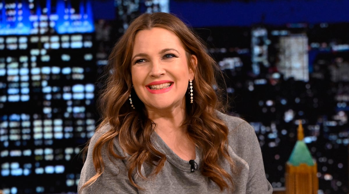 Drew Barrymore smiles and looks on wearing a gray shirt