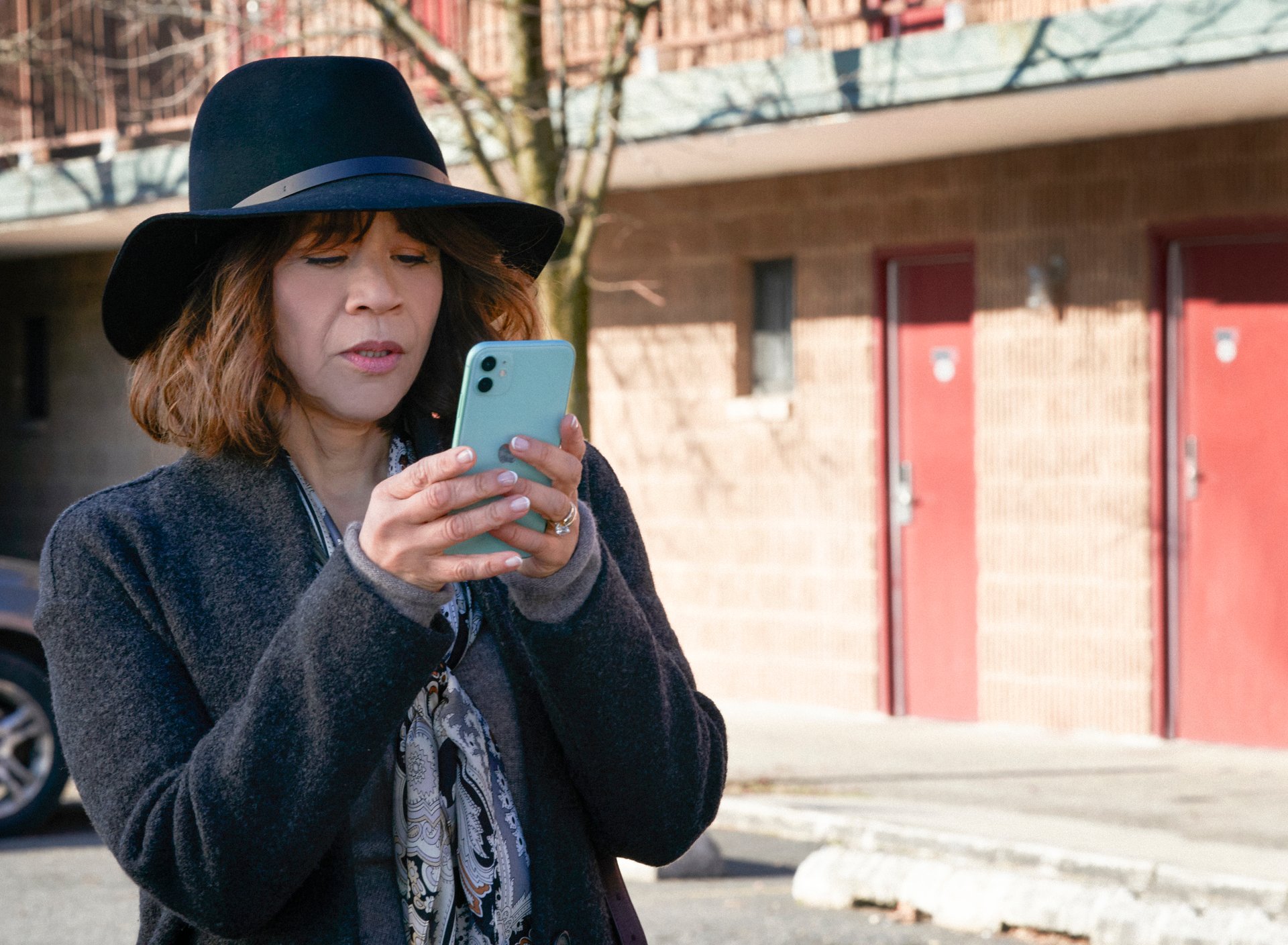 Rosie Perez as Megan Briscoe in 'The Flight Attendant' on HBO Max. She's wearing a black hat and texting on her cellphone.