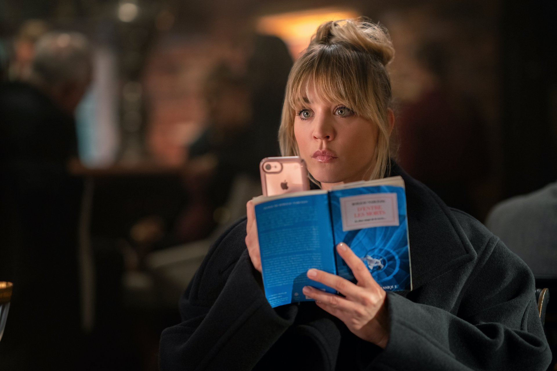 Kaley Cuoco as Cassie Bowden in 'The Flight Attendant' Season 2 on HBO Max. She's recording something on her phone and holding a book up in front of it.